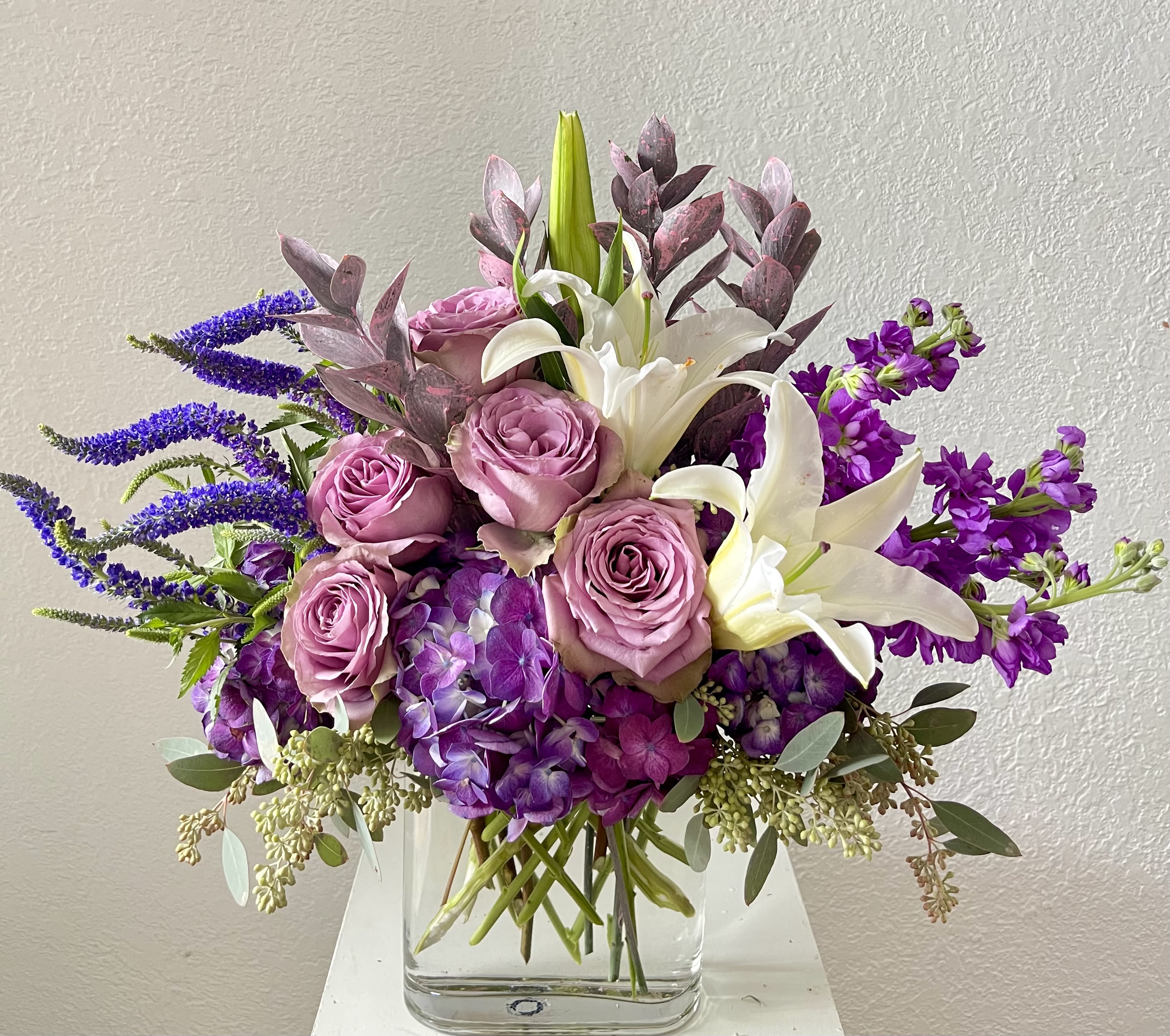 Twilight Garden - Moody, romantic, and full of depth, Twilight Garden is a lush mix of purples and whites designed to evoke the quiet beauty of evening blooms. Featuring rich purple roses, stock, hydrangeas, and Veronica, accented with elegant white lilies, Israeli ruscus, and seeded eucalyptus, this arrangement is artfully arranged in a clear glass vase for a timeless finish.  Handcrafted by Julia’s Floral and available for same-day flower delivery in Dallas, Twilight Garden is a perfect choice for sending elegance with a touch of drama.