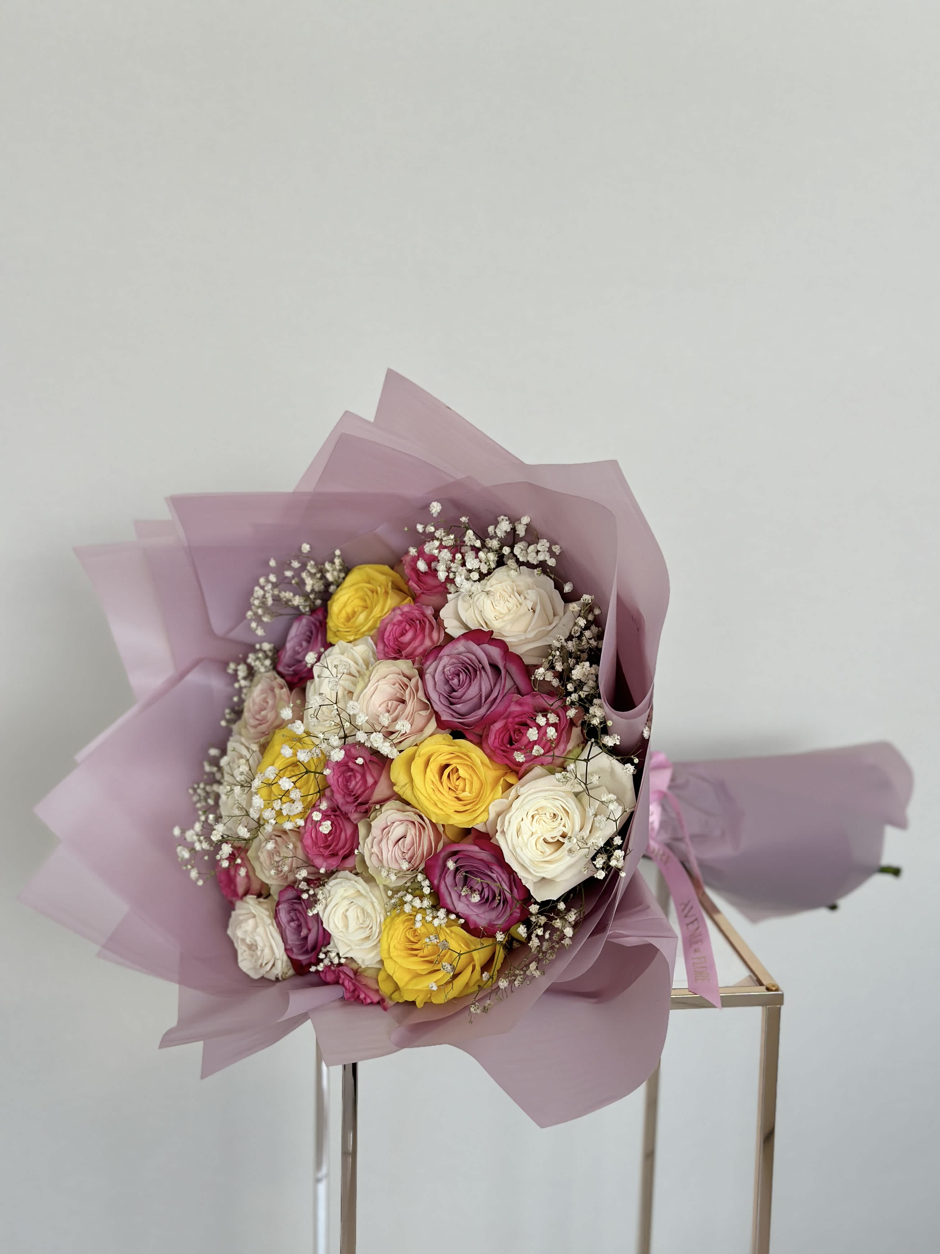 Rainbow Bouquet - A rainbow bouquet bursting with the joyful hues of pink, white, purple, hot pink, and yellow roses. Each bloom, like a painter's brushstroke, adds its unique shade to the canvas of this stunning arrangement. 
