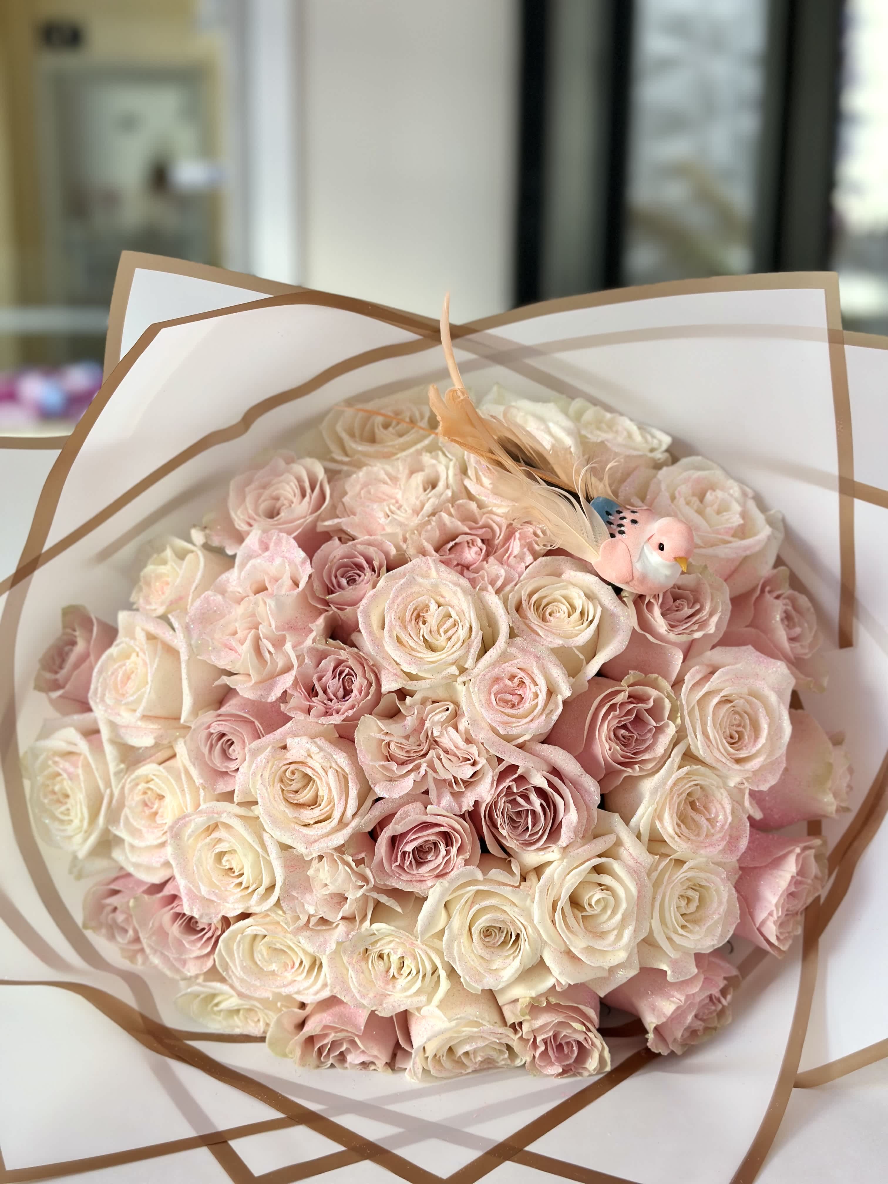 Enchanted Glitter Bouquet - Step into a world of enchantment with our Enchanted Glitter Bouquet, adorned with the delicate detail of a graceful bird. This exquisite arrangement seamlessly blends the timeless beauty of pink and white roses with a touch of magical sparkle. Perfect for those who appreciate the extraordinary, this bouquet is a celebration of love, grace, and a sprinkle of enchanting allure.  