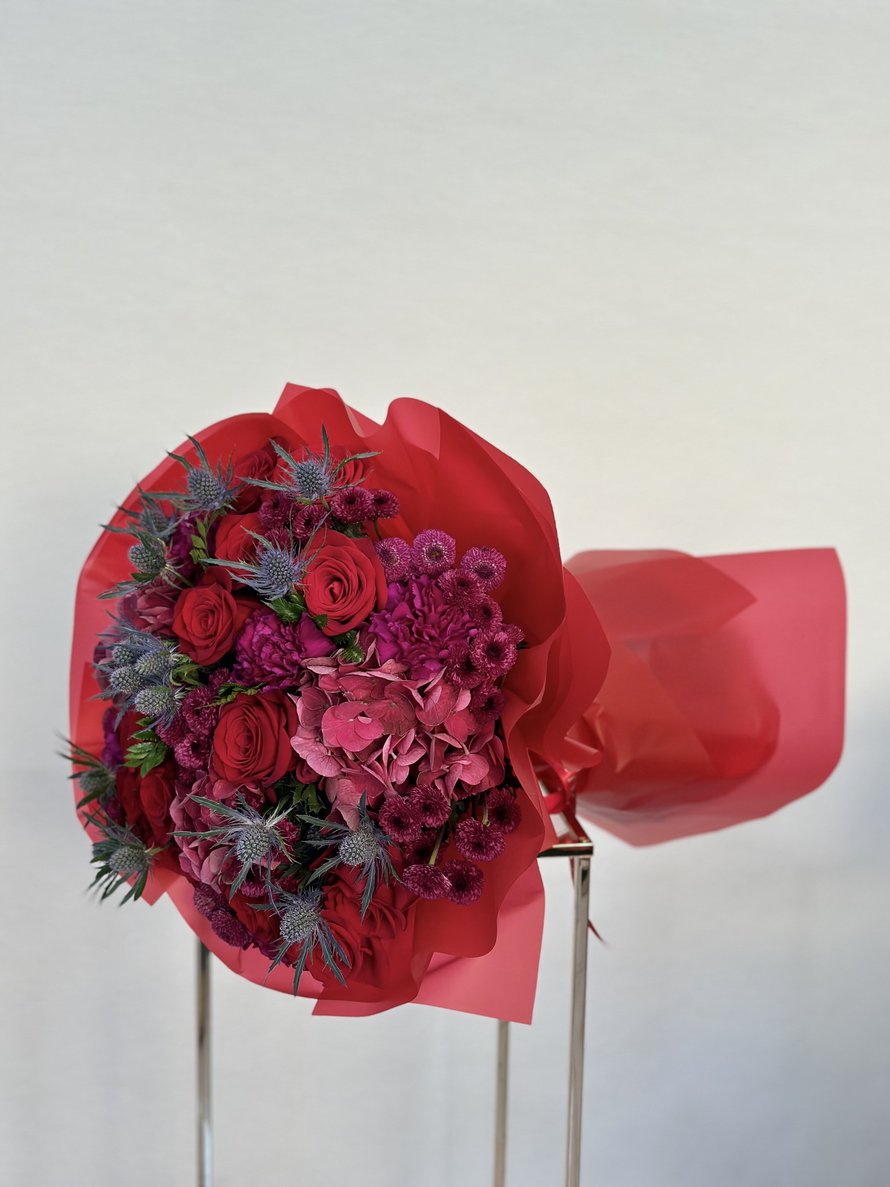 Royal Romance Bouquet - This bouquet is like a vibrant celebration of bold red roses mingling with the whimsical charm of purple hydrangeas. Tucked in between are playful purple chrysanthemums, adding a pop of color and a hint of fun. Whether it's for a special occasion or just to show someone you care, this mix of blooms is sure to spread joy and warmth wherever it goes. 