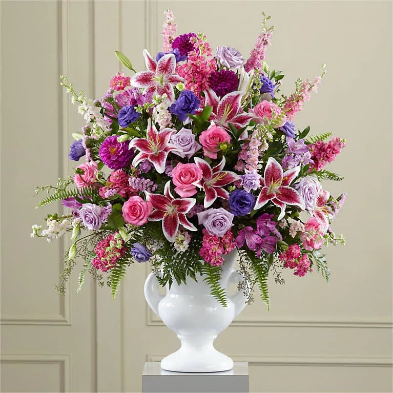 Peaceful Tribute Bouquet - Extravagant, beautiful and comforting, this generously scaled arrangement eloquently expresses your sympathy with an abundance of love and a profound representation of loss. Handcrafted by our artisan designers, it combines a colorful profusion of lavender and hot pink roses, pink statice, purple lisianthus and dahlias, Stargazer lilies and lavender alstroemeria enhanced with a rich and exotic variety of lush greenery in a classically-inspired white ceramic urn. Rose Stock Lily Larkspur Dahlia Alstroemeria
