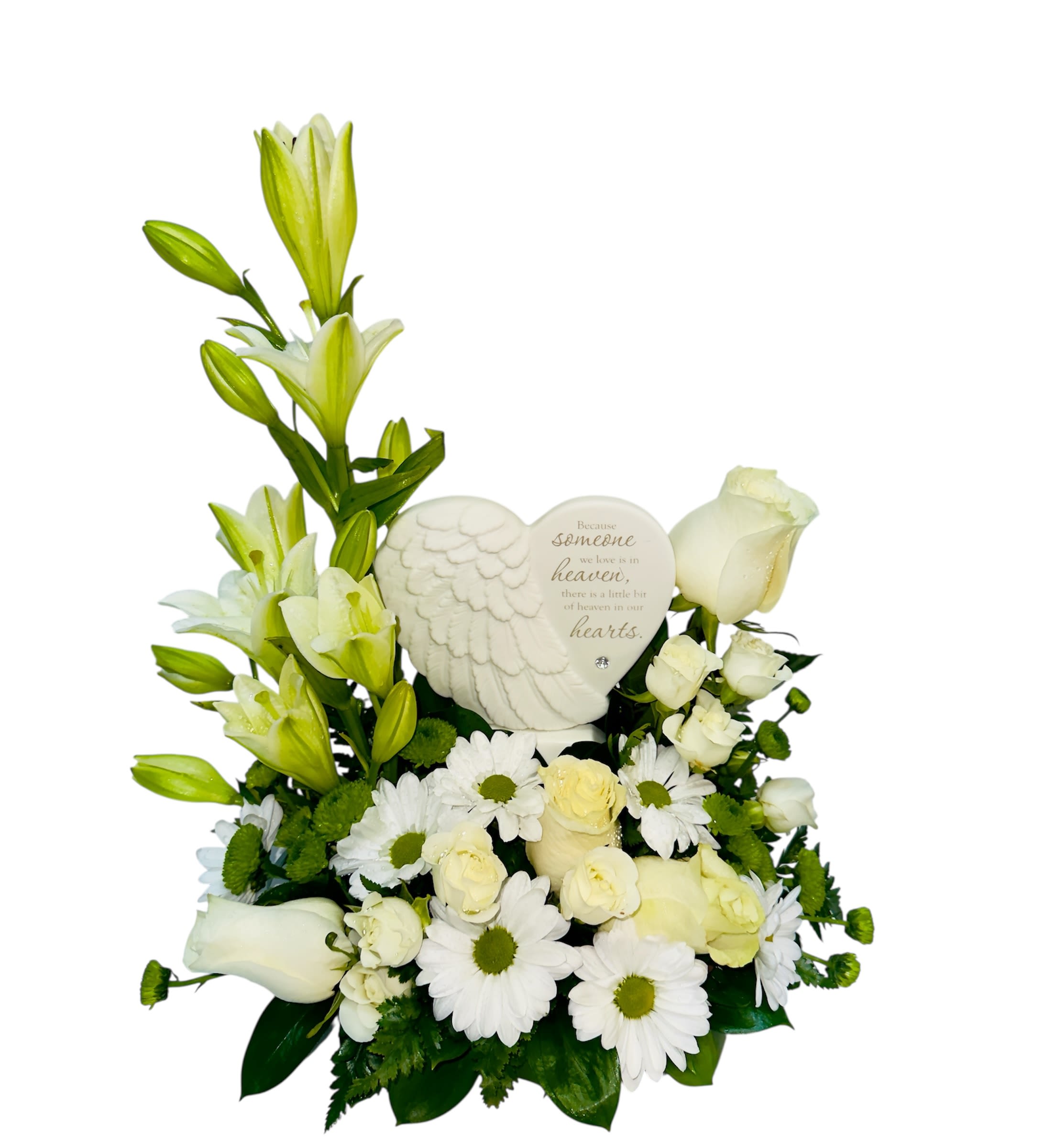 Heaven Embrace  - This serene tribute arrangement speaks with tenderness and remembrance. A graceful mix of white lilies, roses, daisies, and soft fillers surrounds a heart-shaped stone adorned with angel wings and a poignant inscription: *“Because someone we love is in heaven, there is a little bit of heaven in our hearts.”* The design conveys purity, peace, and enduring love—an elegant way to honor cherished memories and evoke comfort.