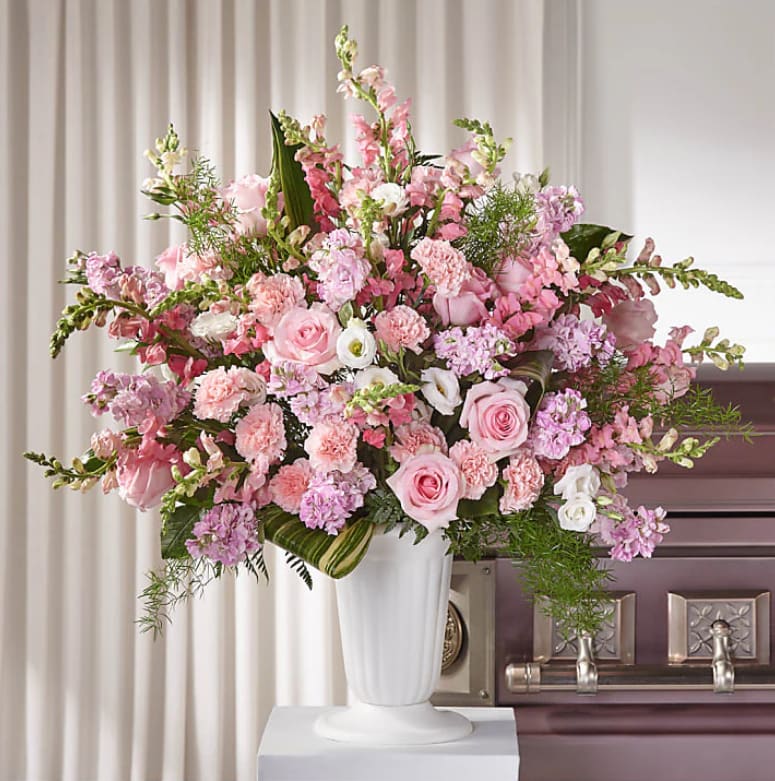 Blushing Elegance Tribute - The Blushing Elegance Tribute is a luxurious and full sympathy arrangement designed to make a graceful statement. Set in a classic white funeral container, this lush display overflows with premium pink roses, soft blush-toned blooms, and elegant snapdragons. Rich in texture and beauty, it’s a heartfelt expression of love, admiration, and lasting remembrance.