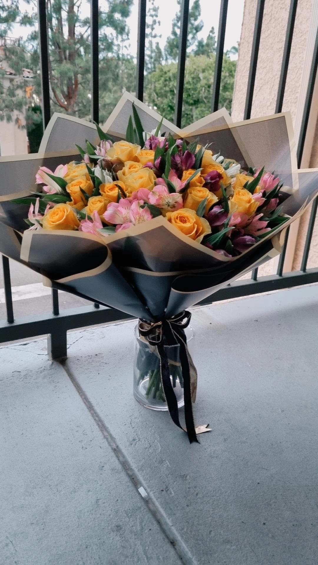 Romantic Serenity -  a stunning bouquet of vibrant yellow roses mixed with delicate pink Alstroemeria flowers, beautifully wrapped in dark and gold-toned paper.  This bouquet can be presented with various color options for the wrapping paper.- Aliso Viejo Florist