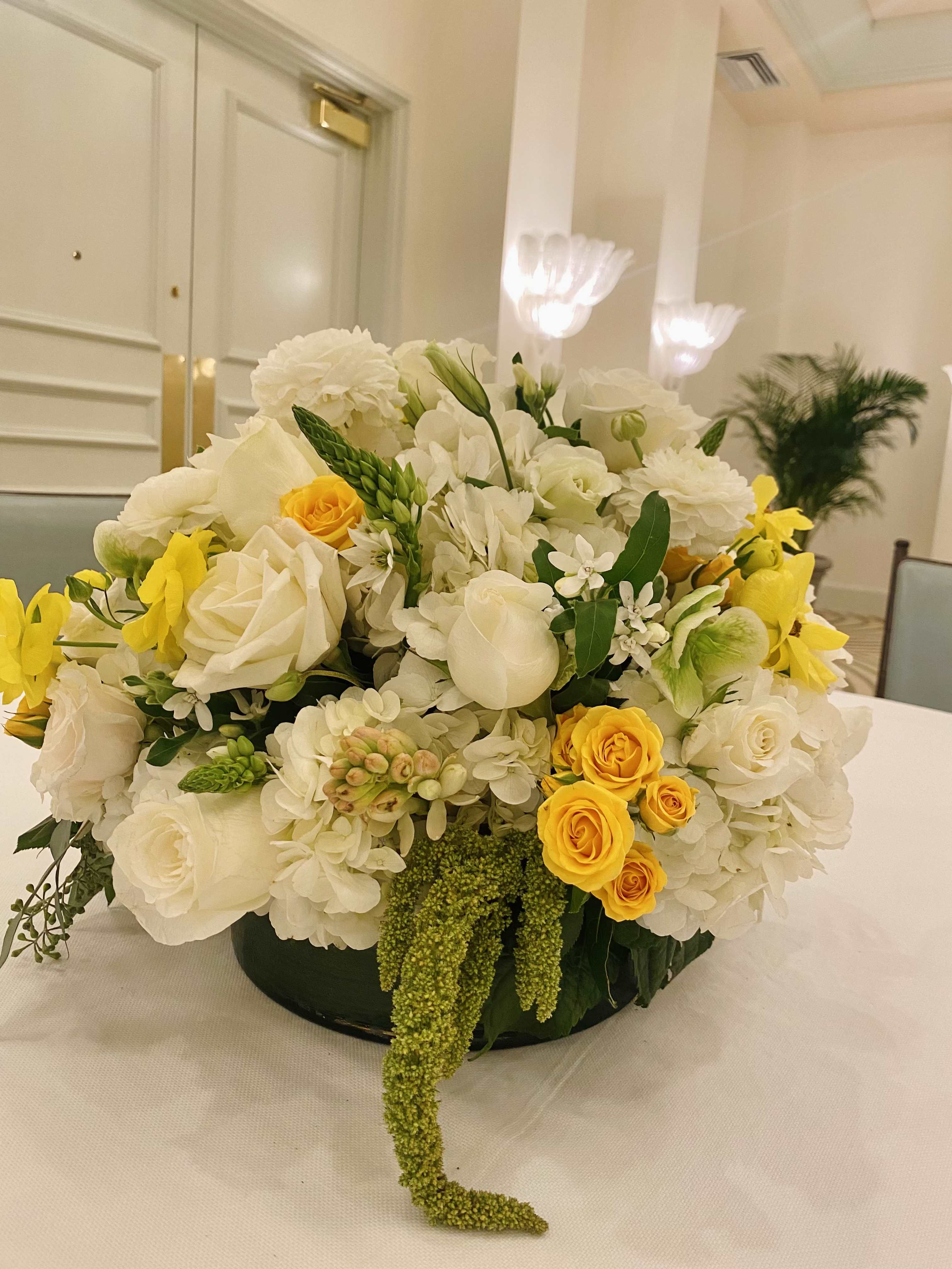 Sun-Kissed Morning - Sunkissed Morning  Brighten any space with the warm glow of Sunkissed Morning, a graceful floral centerpiece that captures the charm of a golden sunrise. This arrangement features soft white hydrangeas, fragrant tuberose, elegant white lisianthus, and romantic white garden roses. Cheerful yellow spray roses bring a burst of sunshine, while a subtle accent of millet adds natural texture and depth. Perfect for special occasions or everyday elegance, Sunkissed Morning brings light and serenity wherever it’s placed.