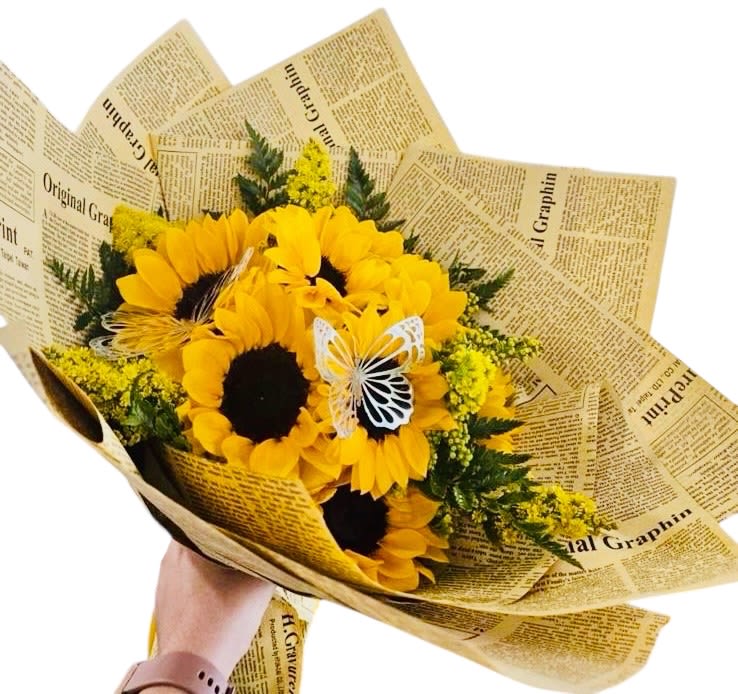 Sun_Kissed Papillon - This bouquet beams with rustic charm and joyful spontaneity. Its brilliant yellow sunflowers—with rich, dark centers—radiate warmth, surrounded by sprigs of vibrant yellow accent flowers and lush green foliage. The newspaper-style wrapping adds a nostalgic, earthy feel, like a love letter from the countryside, while two delicate butterflies perched among the blooms infuse whimsy and a touch of symbolism—transformation, freedom, and fleeting beauty. It's cheerful yet thoughtful, perfect for heartfelt gestures with a cozy, handcrafted flair.