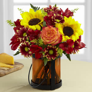  Giving Thanks - Exuding a superior warmth and sophistication, this gorgeous flower bouquet will be just the gift to send to become a part of your special recipient's fall celebrations! Stunning sunflowers are bold and beautiful when combined with bi-colored orange roses, red Peruvian lilies, yellow solidago, burgundy traditional daisies and lush greens, perfectly brought together to create an unforgettable flower bouquet. Presented in an orange glass vase.