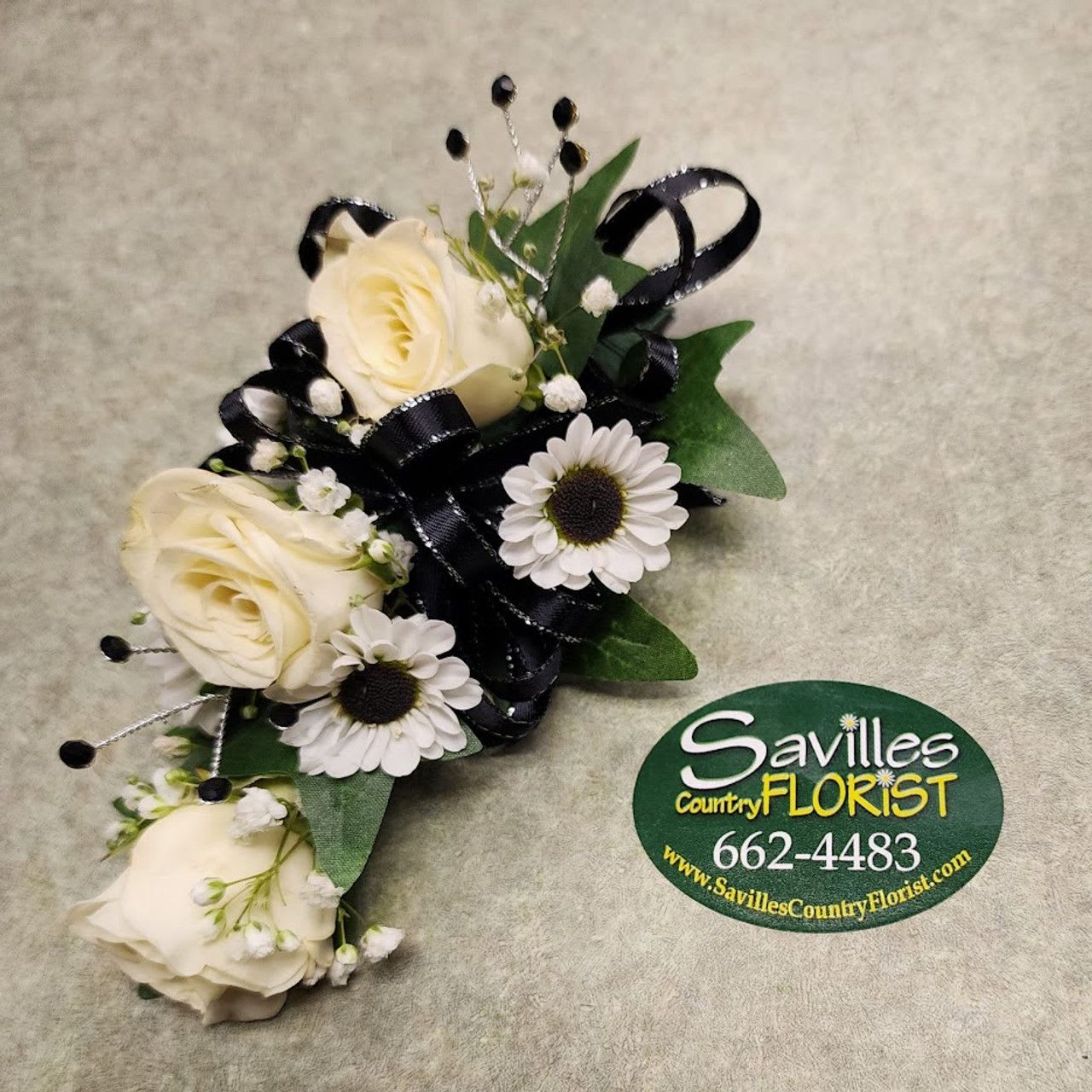 The Classy Corsage The Classy Corsage - The Classy Corsage by Savilles Florist features a corsage with 3 white roses, 4 yin yang daisies, babies breath, black gems and a black & silver bow