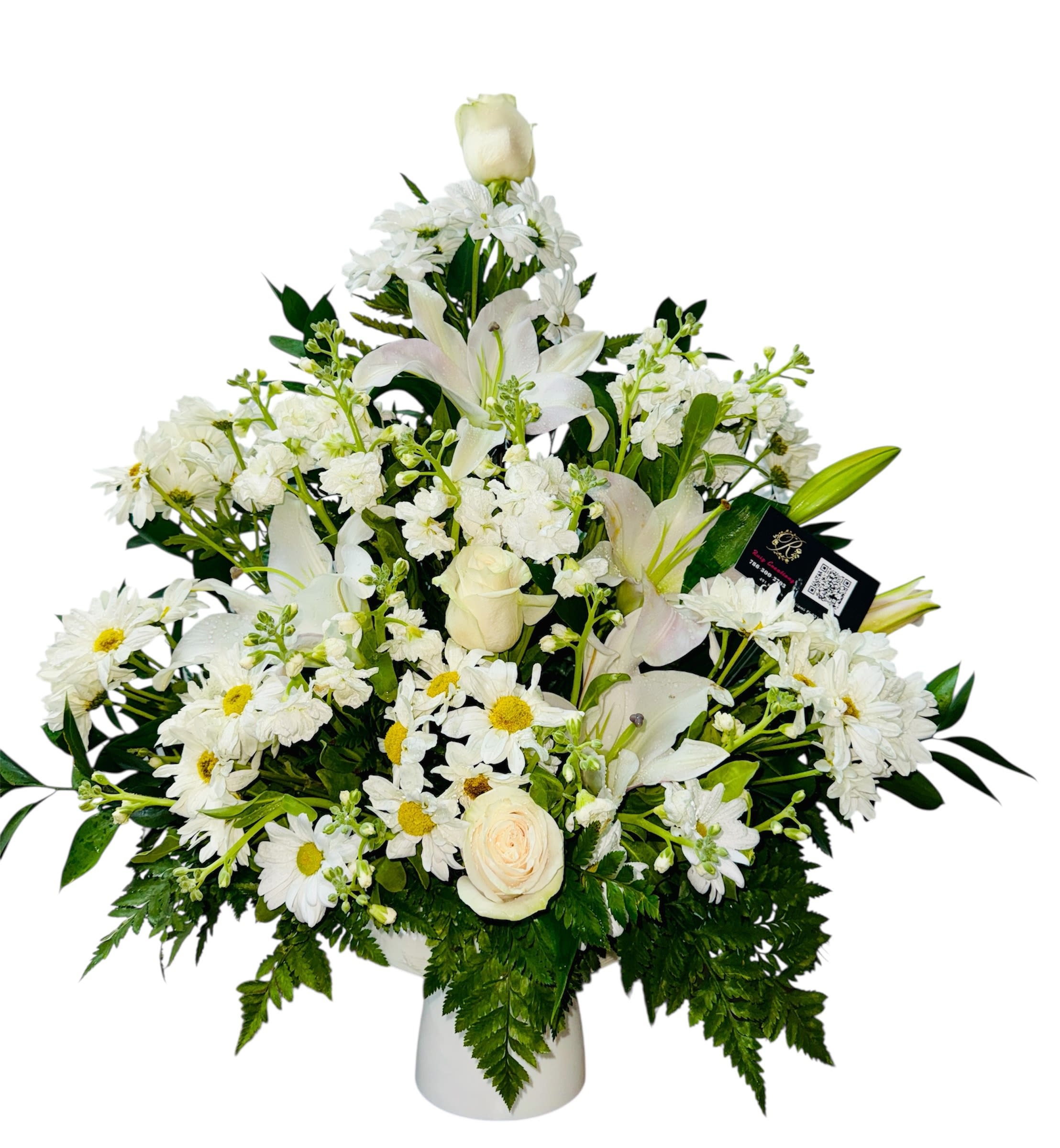 Ivory Serenade - This serene white arrangement sings with timeless elegance. A harmonious blend of white roses, lilies, daisies, and petite filler blooms creates a soft, layered texture that evokes purity and peace. The crisp white vase anchors the bouquet in simplicity, while the rich green foliage adds contrast and depth. A sleek black tag with a QR code nods to modern touches—perhaps a portal to your story or brand essence.  Perfect for weddings, sympathy gestures, or sophisticated events, this arrangement is a quiet symphony of grace and intentionality.