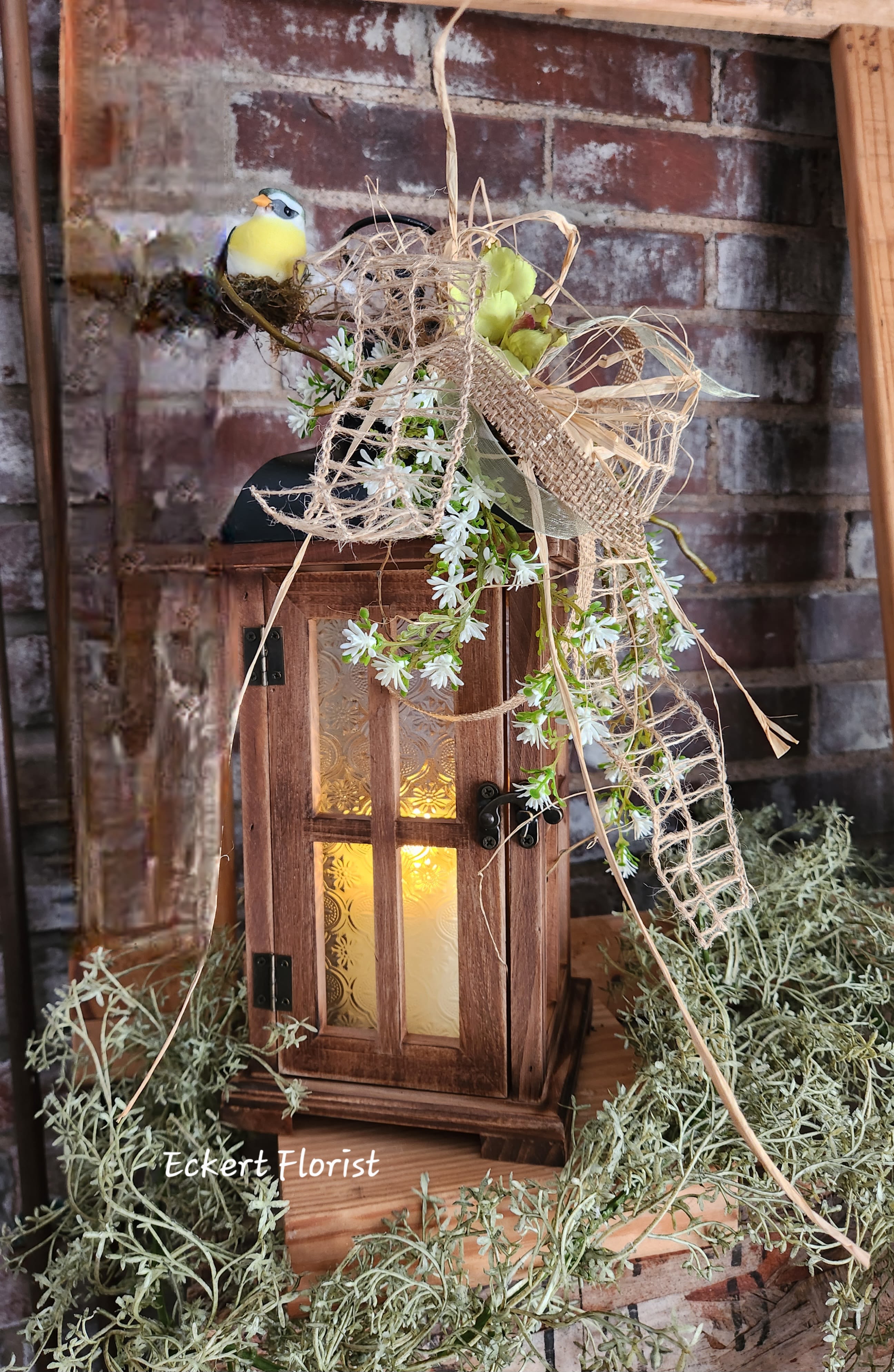 Eckert Florist's Small Brown Textured Glass Lantern *Our Local Delivery Only Eckert Florist's Small Brown Textured Glass Lantern *Our Local Delivery Only - This brown wooden lantern arrives with textured glass, battery operated candle, floral decor and designer ribbon. Our signature twigs and bird is also included. Lantern measures approx. 16" High x 5.5" Square. Batteries are included. *Our Local Delivery Only