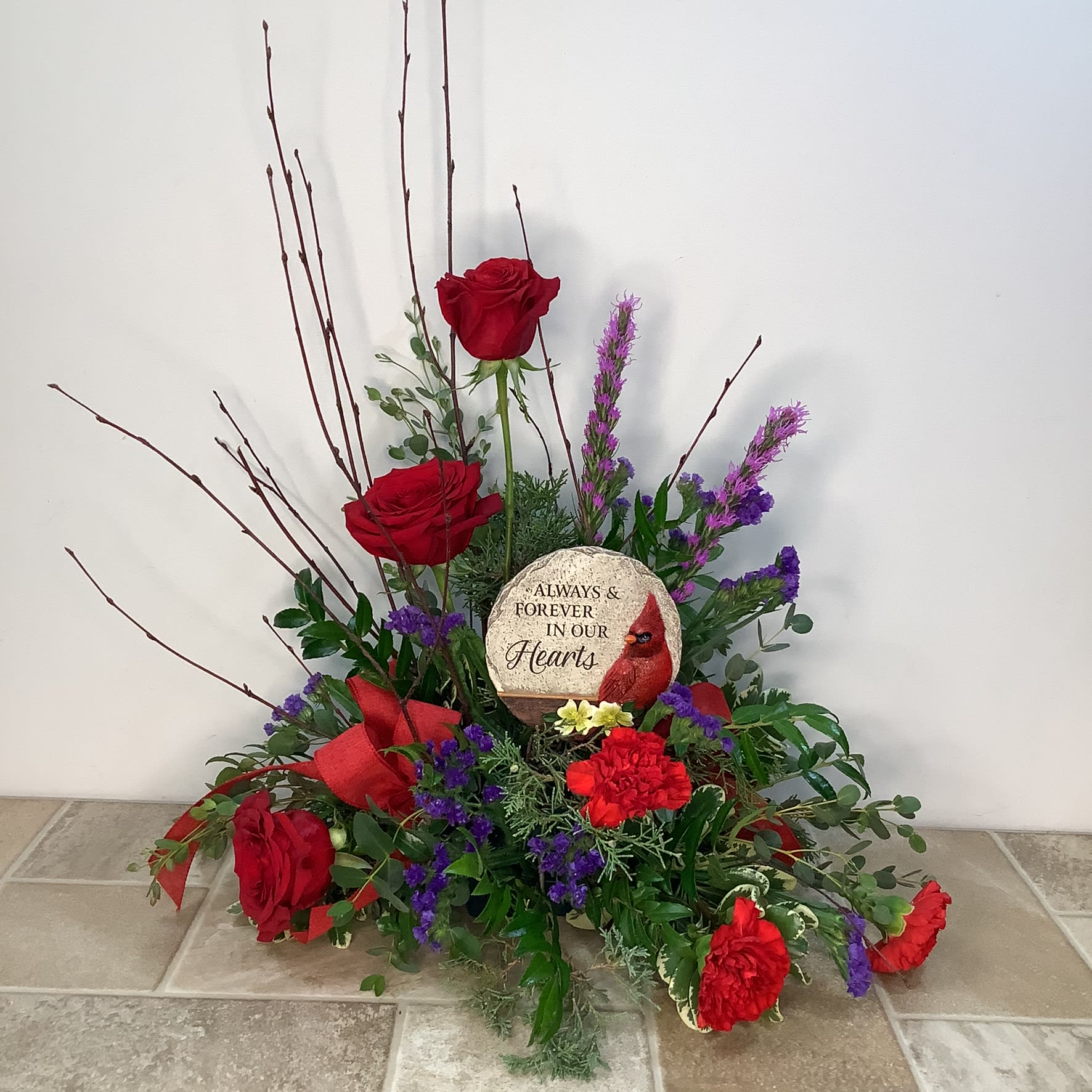 With Sympathy With Sympathy - A stylish arrangement featuring red roses and carnations, liatris and purple static. It holds a keepsake stone that will perfectly express your deepest sympathy. It measures 20” wide x 22” tall.