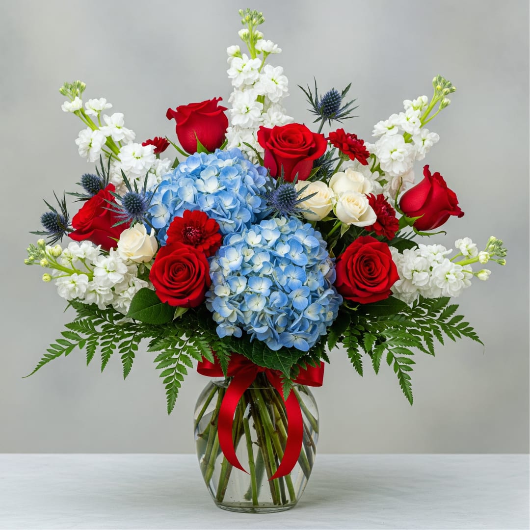 America the Beautiful America the Beautiful - Send a grand tribute with our American the Beautiful arrangement! This patriotic design bursts with vibrant red, white, and blue, perfect for celebrating national holidays, honoring service, or showcasing your American pride with breathtaking style. This magnificent display features classic red roses, lush blue hydrangeas, and crisp white stock flowers, all brilliantly accented with blue thistle that evokes the dazzle of fireworks. Adorned with a sophisticated red satin bow and proudly presented in a traditional clear glass rose vase, creating a timeless and impactful centerpiece. Let us help you send an unforgettable expression of patriotism and beauty. Order the America the Beautiful bouquet today and celebrate with unparalleled grace.
