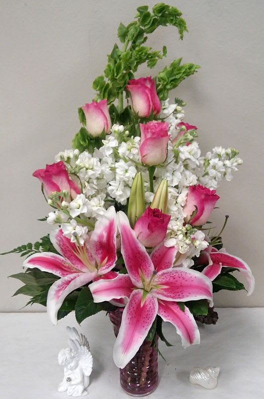 In The Pink - Pink roses, white stock, bells of Ireland with pink lilies made in an intriguing glass designer art vase which may vary according to availability and the occasion.