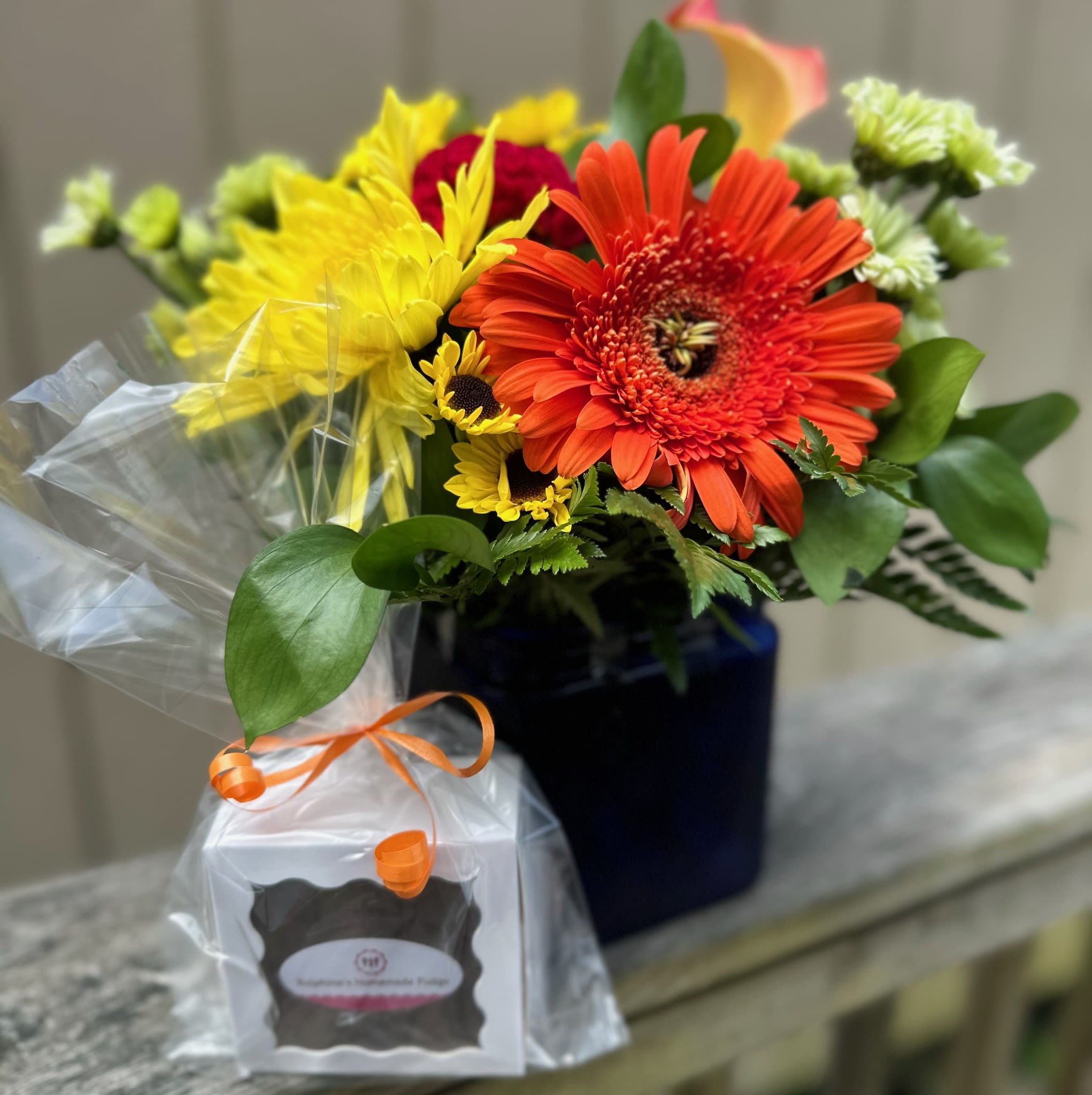 Deal of the Day Sunburst Bqt with Fudge - Orange gerbera, calla lily, carnations, alstromeria, yellow poms, green daisies and hydrangea with red solocia in a blue cube vase with Ralphina's homemade fudge.