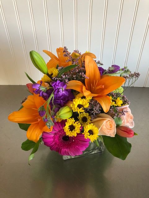 Compacte Designer's Choice - In a low, square, glass vase, this arrangement will include seasonal blooms and greenery which may or may not include the flowers pictured. If you have specific wants for the arrangement please leave a note at checkout and we will try to include your special requests.