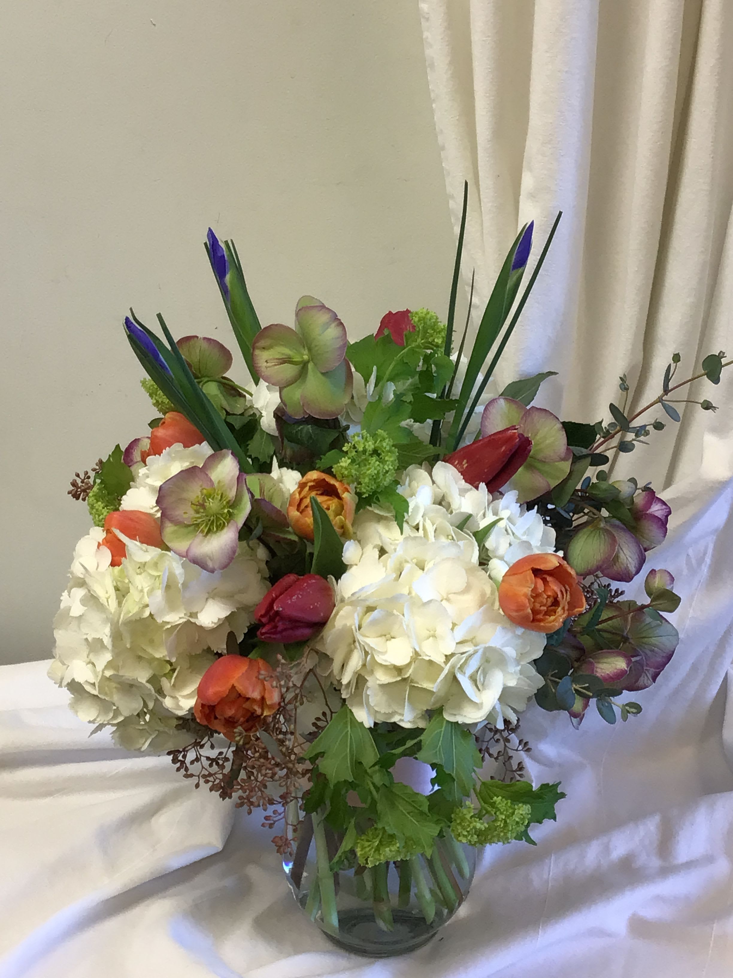 Sing into Spring Sing into Spring - You feel like inviting spring into your home with this arrangement. It makes you want to sing! Spring flowers such as tulips, Irises, Viburnum, and hellebores are delightfully arranged in a classic glass vase.