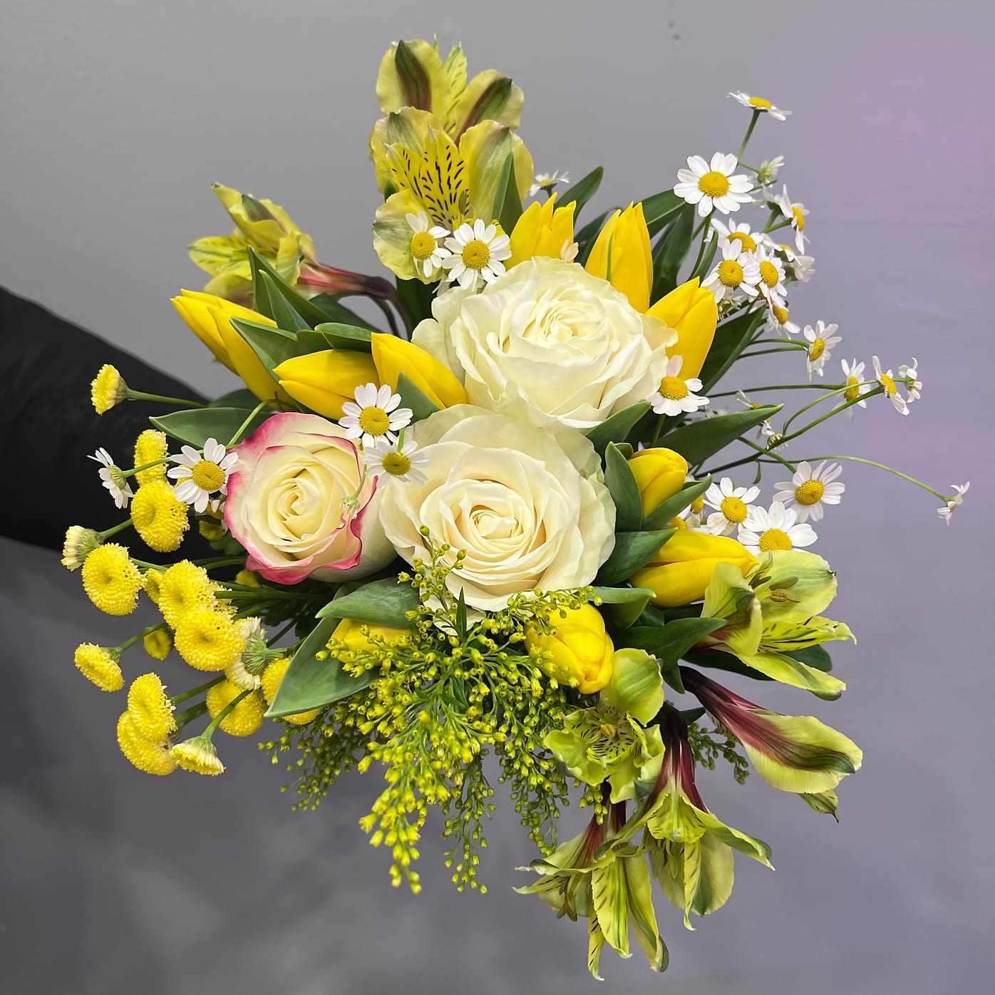 Spring Bouquet Deluxe - A radiant little arrangement of yellow tulips, creamy garden roses, and daisy-like blooms, “Spring Bouquet Deluxe” is a celebration of the quiet kind of happiness—the kind that shows up without fanfare, like sunlight through the blinds or laughter in the kitchen. It's joyful, unfussy, and made to lift spirits. For new mornings, warm welcomes, and just-because smiles.
