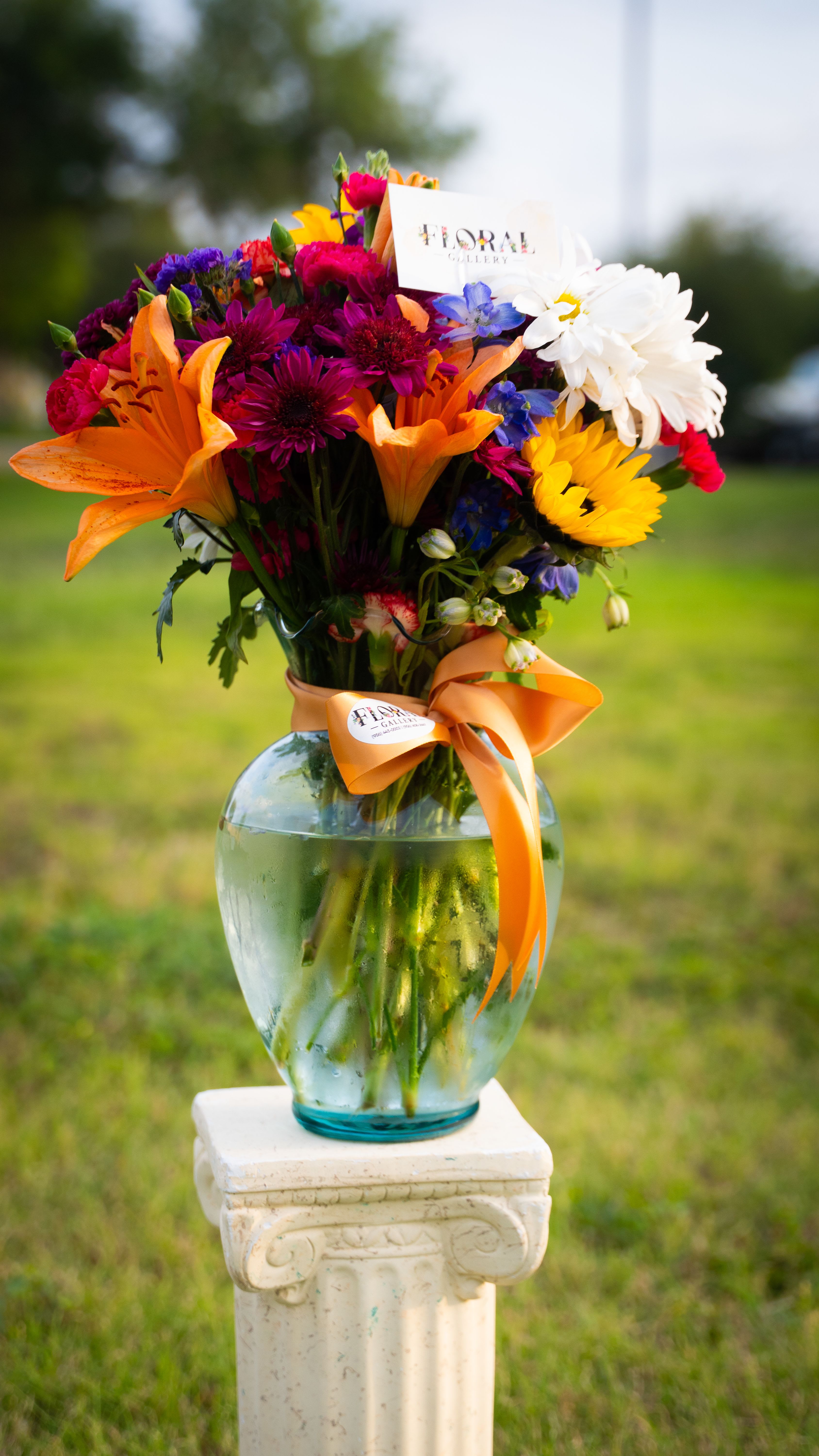 Golden Meadow Symphony by Floral Gallery Golden Meadow Symphony by Floral Gallery - Bursting with charm and warmth, Golden Meadow Symphony is a lush, radiant celebration of nature's brilliance. This stunning arrangement blends the cheerful faces of white daisies and golden sunflowers with the playful textures of pompoms and the soft, rustic elegance of statice flowers. Perfectly full and beautifully balanced, it's a vibrant display that evokes the serenity of a sun-kissed meadow in full bloom—inviting joy, comfort, and timeless beauty into any space.