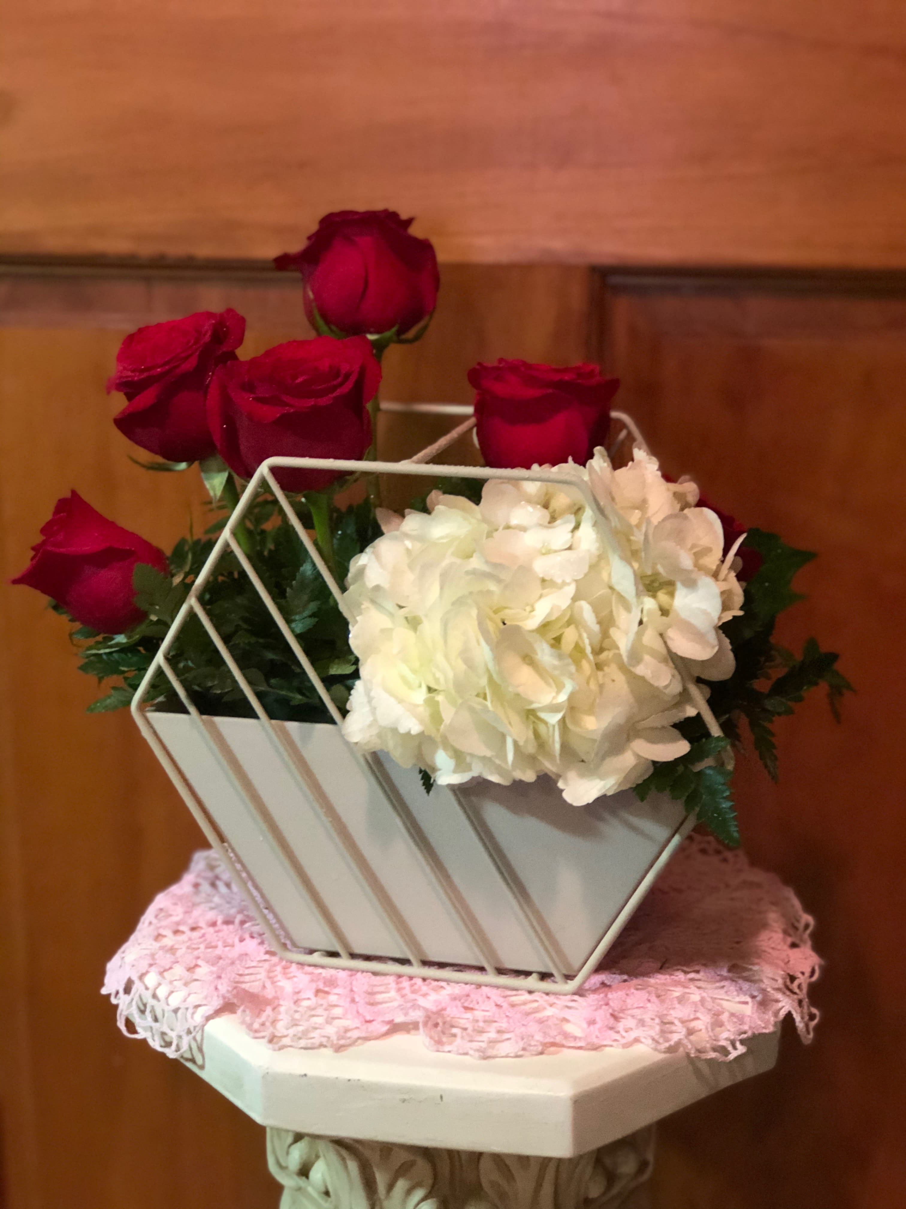 Secret Garden - Our Secret Garden comes with two purposes, first comes the blooms. One Large Hydrangea (could be blue or white) is perfectly paired alongside 6 red roses with leatherleaf fern. After the blooms had faded, the second use comes into effect. Empty out the flowers and foam and you have a wonderful 2 piece planter that can be hung on the wall with any kind of plant you wish to display. Hole is pre-drilled into the hanging planter. Size: 8.75 x 4.75 x 7.75  Inventory control: 3