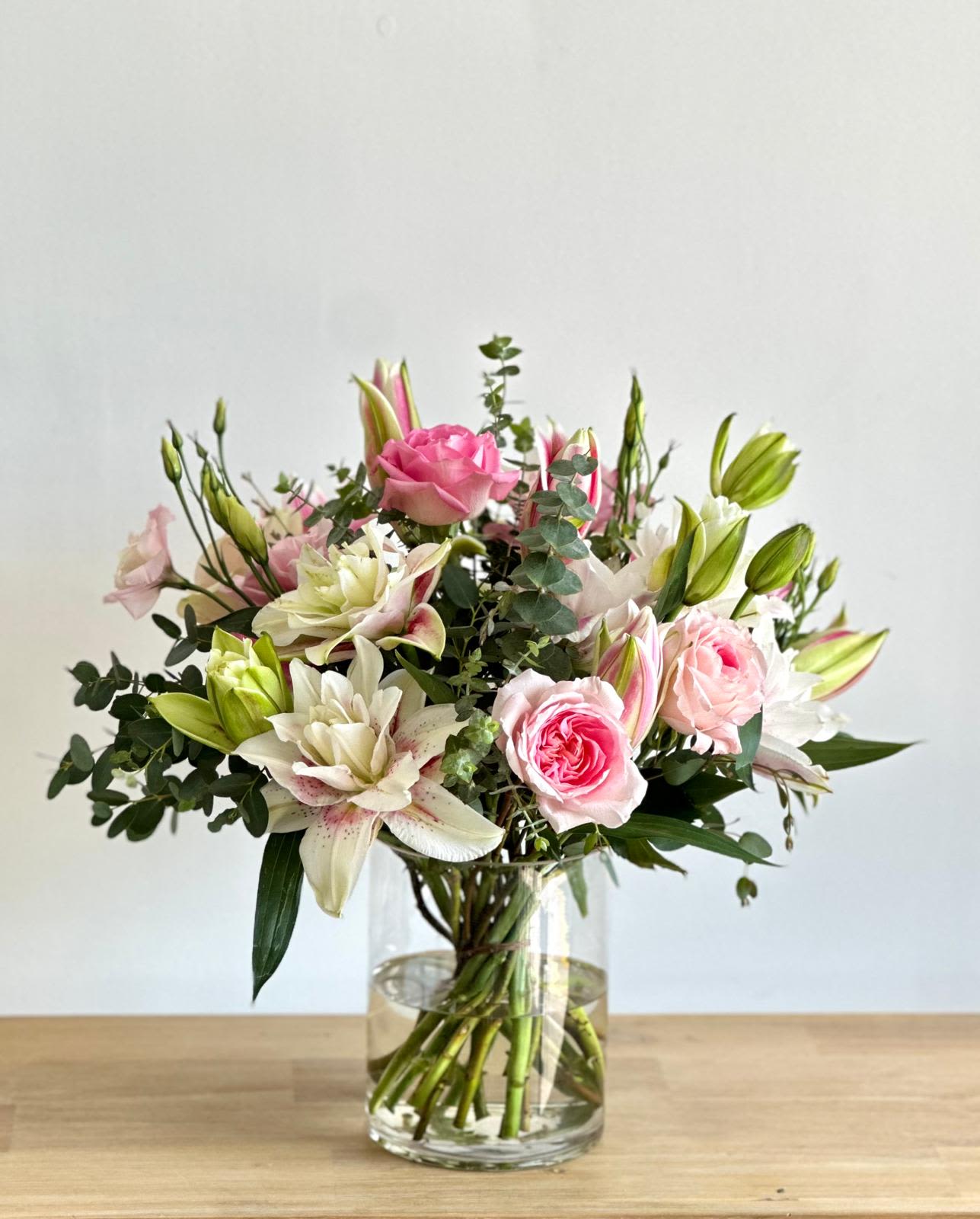 Honey Mom Honey Mom - A medium cylinder glass vase with pink and white flowers and fresh greenery. Flower types may vary depending on the season.