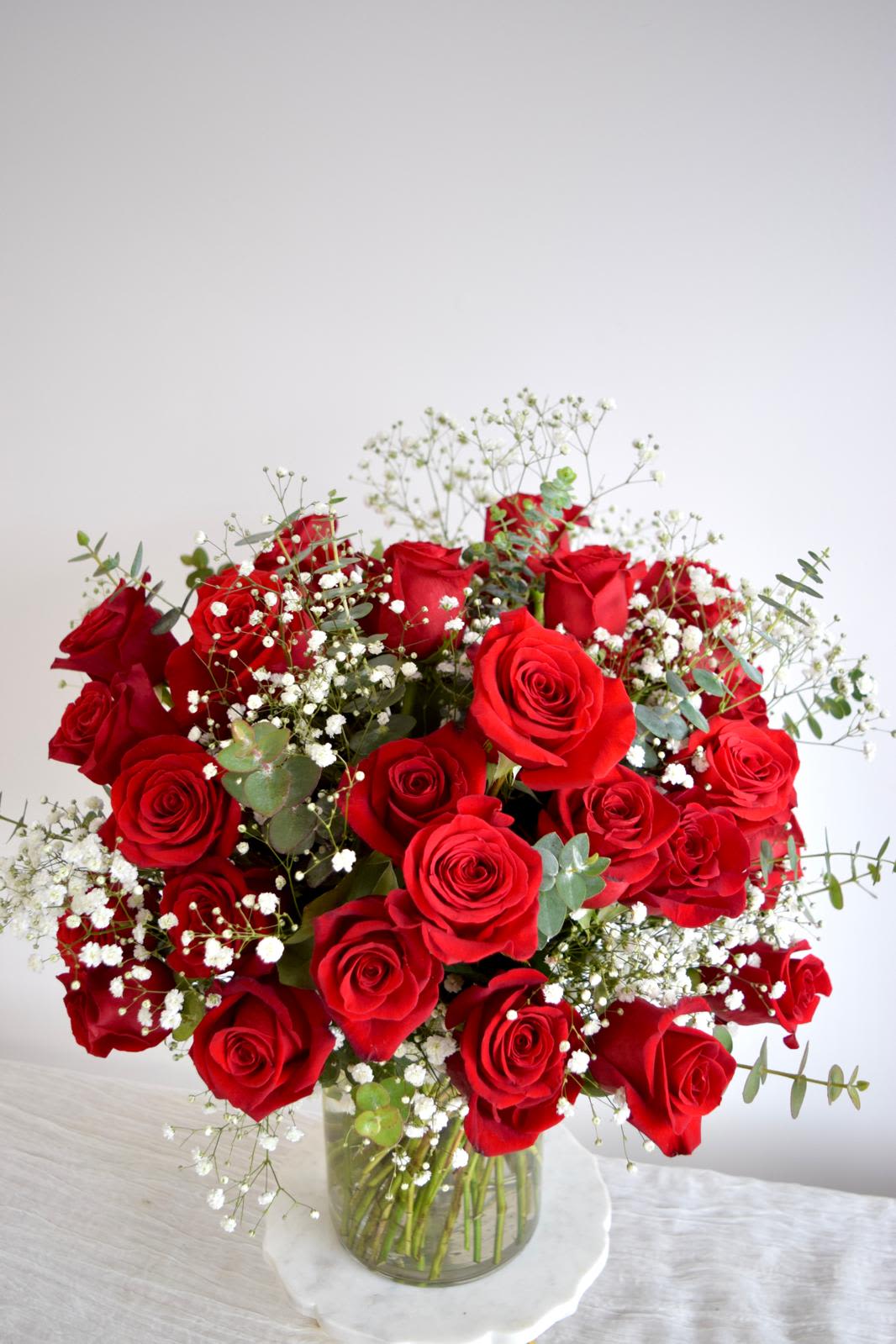 New Romantic  - A medium cylinder glass vase with red roses, baby's breath, and eucalyptus.   Flower types may vary depending on the season.