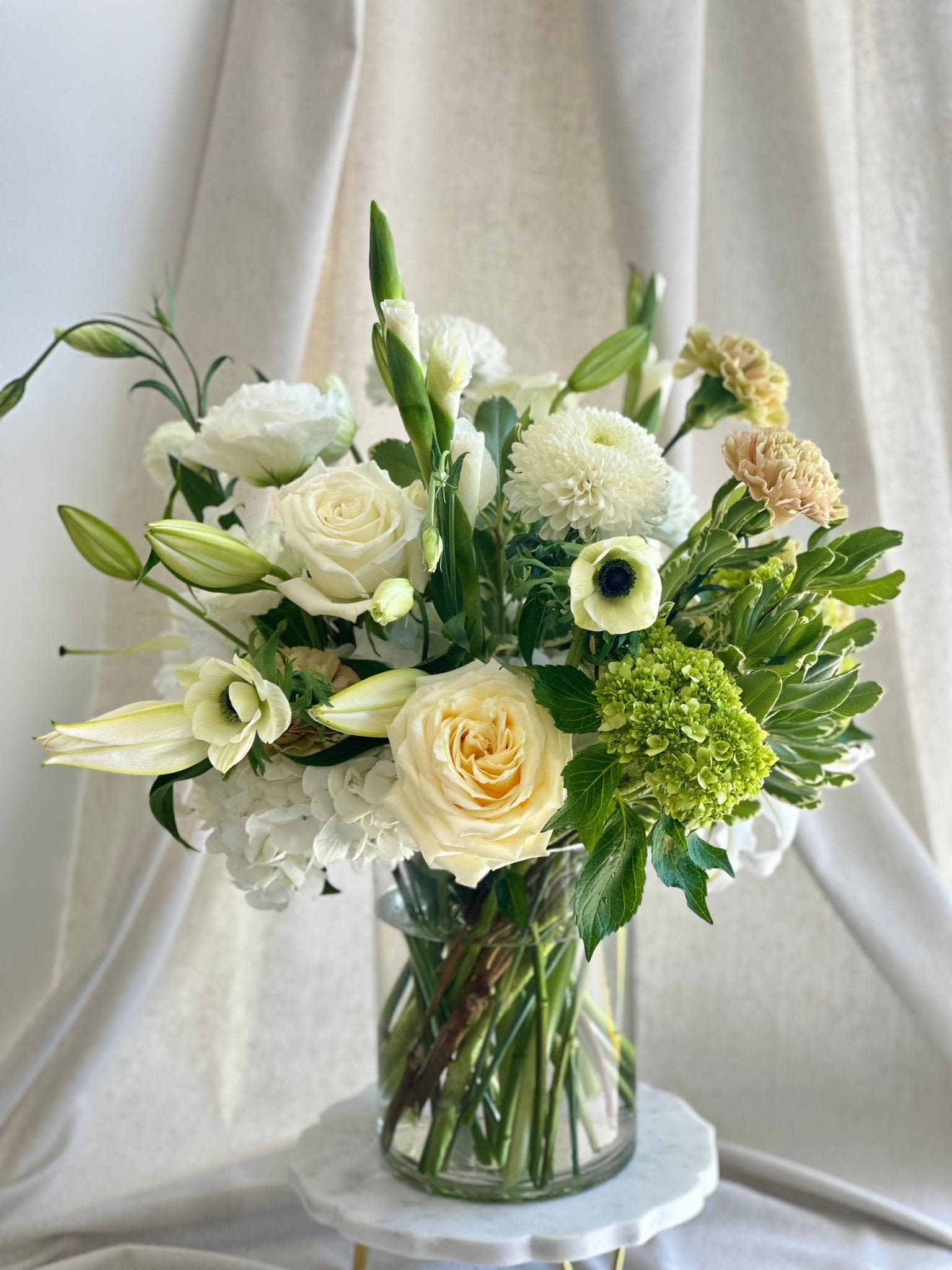 Serene Elegance  - A medium-tall cylinder glass vase with white, brown, and green flowers.   Flower types may vary depending on the season.