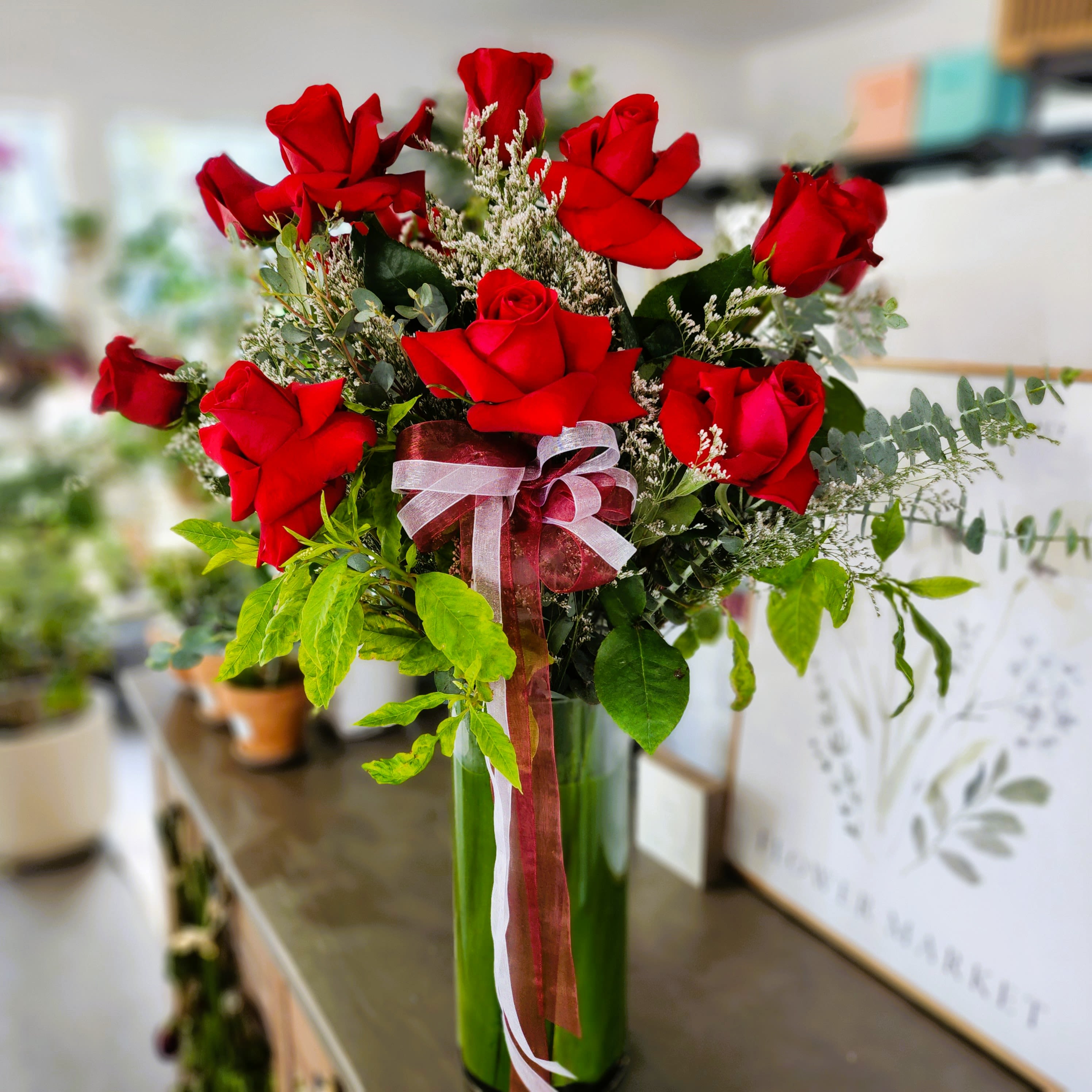 1 Dozen Red Rose - Romantic Red Rose One Dozen with Greenery and Filler in a tall clear vase.  Deluxe: 18 Roses. Premium: 2 Dozen Roses.