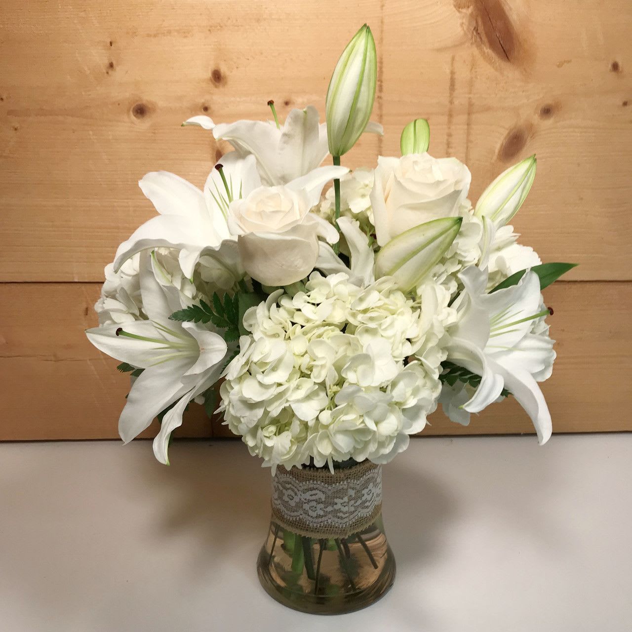 Heaven Scent - An absolutely beautiful presentation of soft whites that would be fitting to give for any occasion.  White roses, lilies and hydrangea are all skillfully arranged in a clear glass vase and accented with a lace sleeve over the vase.  Approx. 18&quot; H x 12&quot; W.  Available for delivery locally to Buffalo, NY and the surrounding suburbs.  