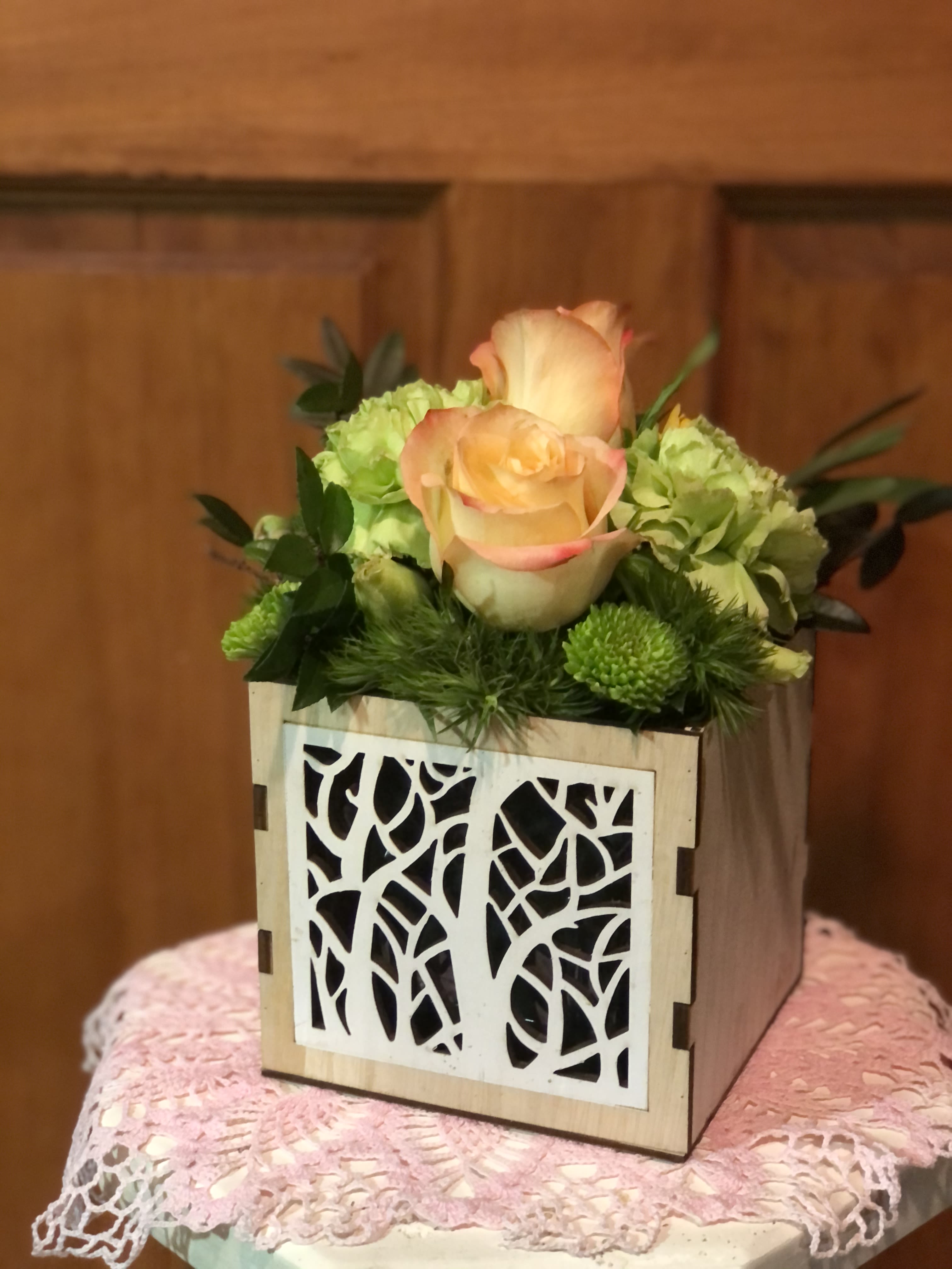 Leaf Shadows  - Shadows of leaves cut out in a natural wooden cube. Fun, festive and fashionable, this design paired with the freshest of roses and/or carnations, accented with spray chrysanthemums, green trick dianthus and fresh greens round out this eye-catching colors of bright green and soft yellow. NOTE: (Florist choice of 3 different designs cubes.)