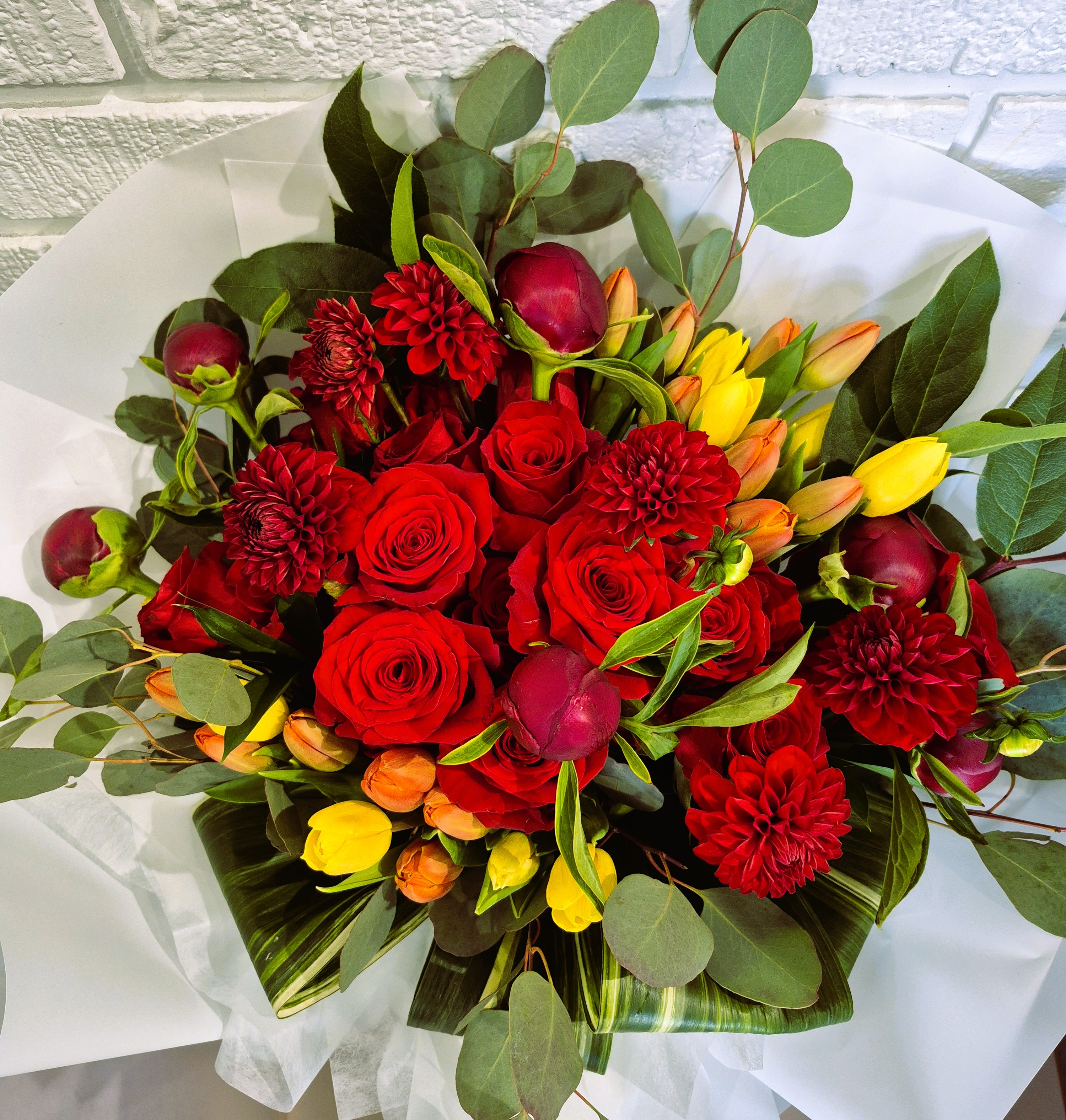 Hug me - Burgundy Peonies, Red Roses, Orange tulips and Yellow tulips with greenery hand bouquet.
