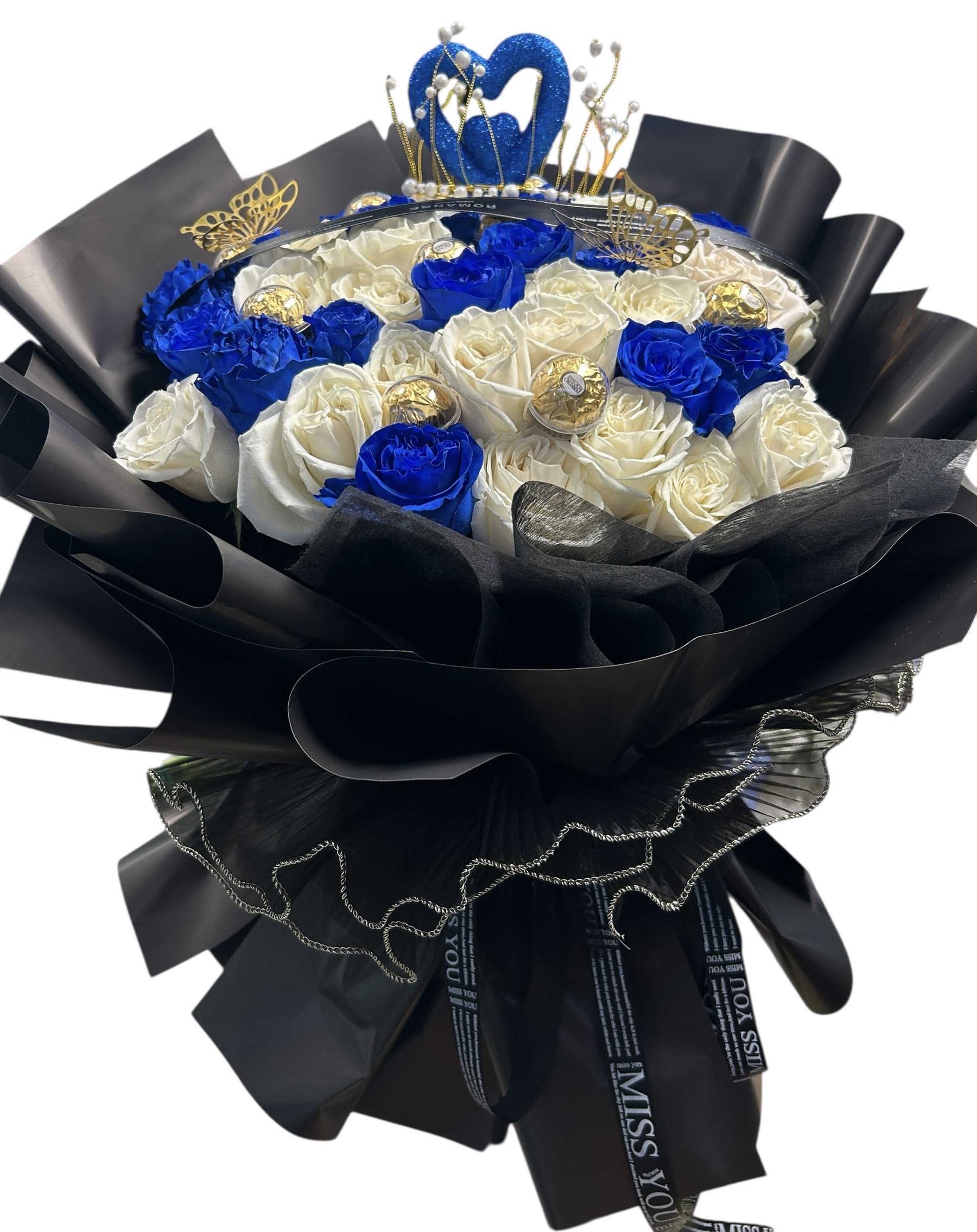 Royal Heart Royal Heart - Elegance meets romance in this luxurious bouquet featuring a stunning blend of deep royal blue and pure white roses. Adorned with golden butterflies, Ferrero Rocher chocolates, and crowned with a sparkling heart-shaped tiara, Royal Heart is a tribute to timeless love and graceful beauty. Wrapped in dramatic black and gold with delicate ribbon details, it makes the perfect statement for someone truly special. Whether it’s a romantic gesture or a heartfelt celebration, this bouquet turns moments into memories.