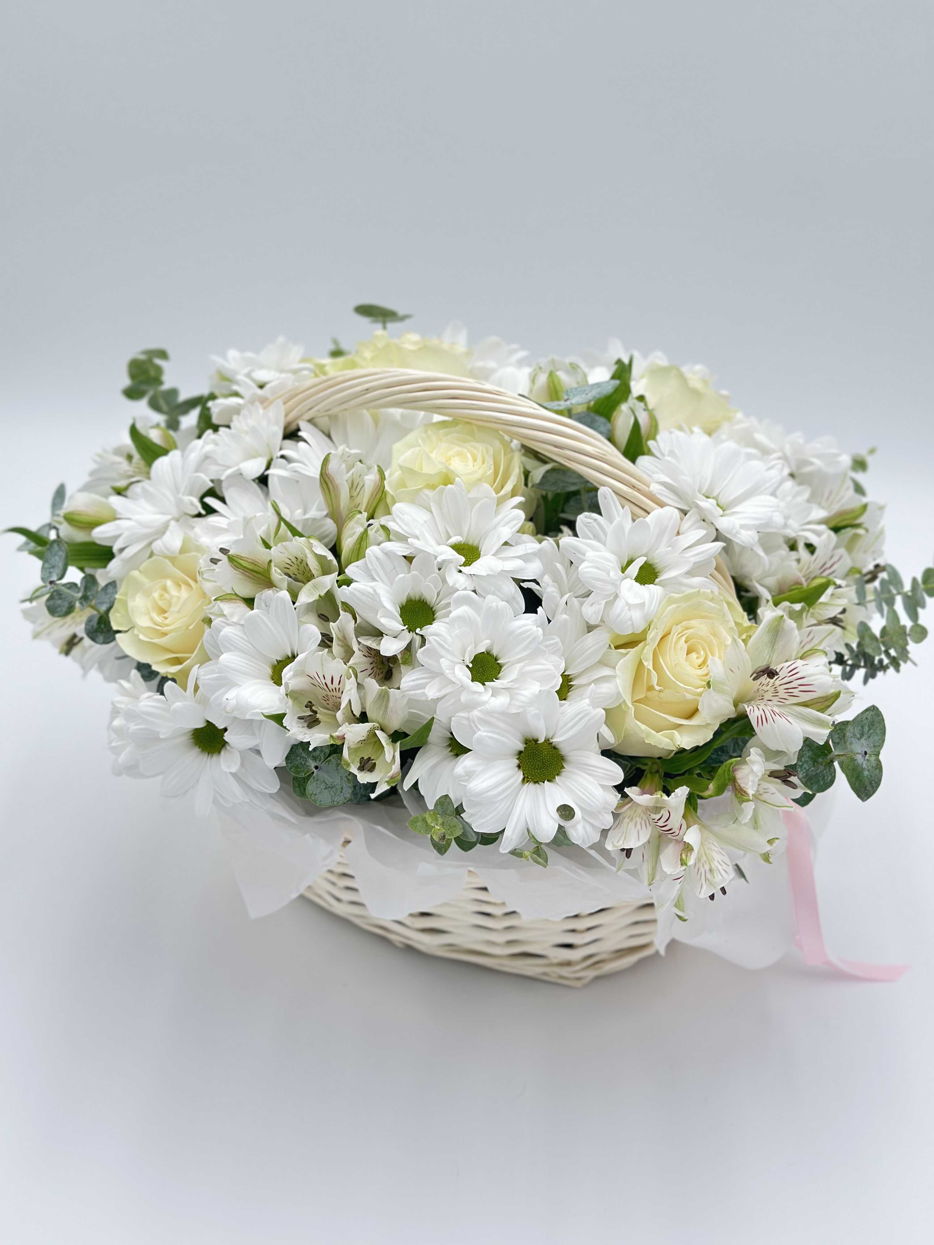 White Bloom - A small basket full of tenderness — white roses and daisy-like chrysanthemums entwine in a pure, luminous duet. The roses add elegance, while the soft, simple petals of the chrysanthemums evoke summer fields and carefree days. Fresh eucalyptus sprigs bring a gentle scent and a touch of green freshness, perfectly balancing the white palette.  This basket is a quiet joy: subtle, touching, and full of warmth. A perfect gift to say: “You are the light.”