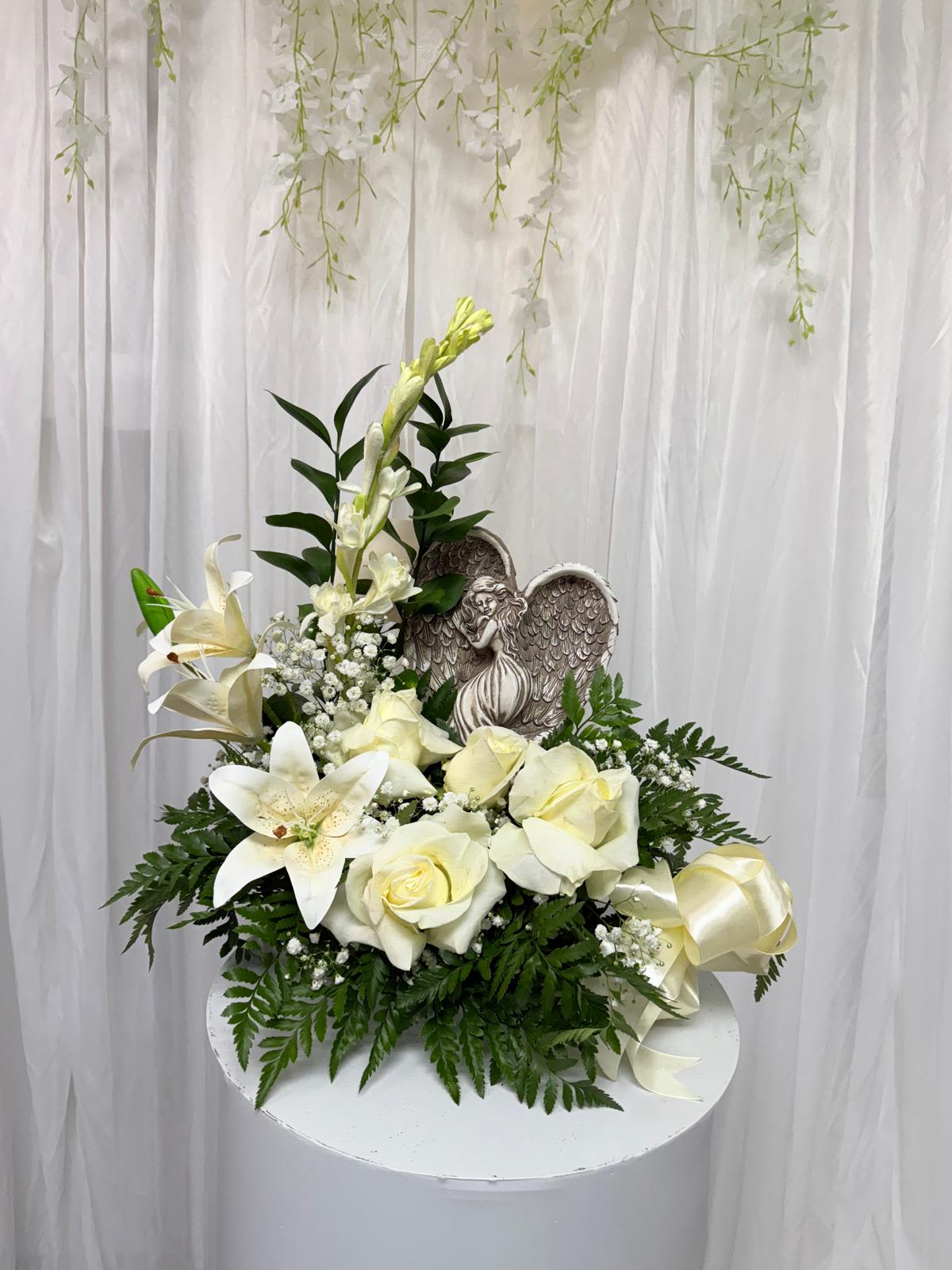 Heavenly Light by Clarita's Heavenly Light by Clarita's - A serene arrangement featuring white roses, lilies, and greenery, adorned with an angel figure. Perfect to convey peace, hope, and comfort during meaningful moments.