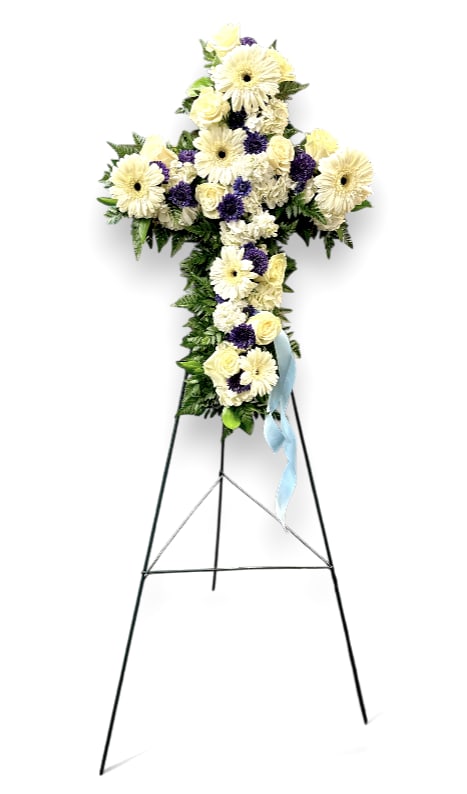 Blue Serenity Memorial Easel - The &quot;Blue Serenity Memorial Easel&quot; is a beautifully crafted tribute designed in the shape of a cross, symbolizing faith and hope. Adorned with a delicate arrangement of white gerbera daisies, soothing blue ocean mums, soft white roses, and elegant white hydrangeas, it creates a peaceful and comforting display. These flowers rest on a lush bed of mixed greens, adding depth and vibrancy to the arrangement. A gentle baby blue bow accents the easel, enhancing its serene and calming presence. This memorial easel serves as a heartfelt tribute, offering a sense of tranquility and remembrance for loved ones.