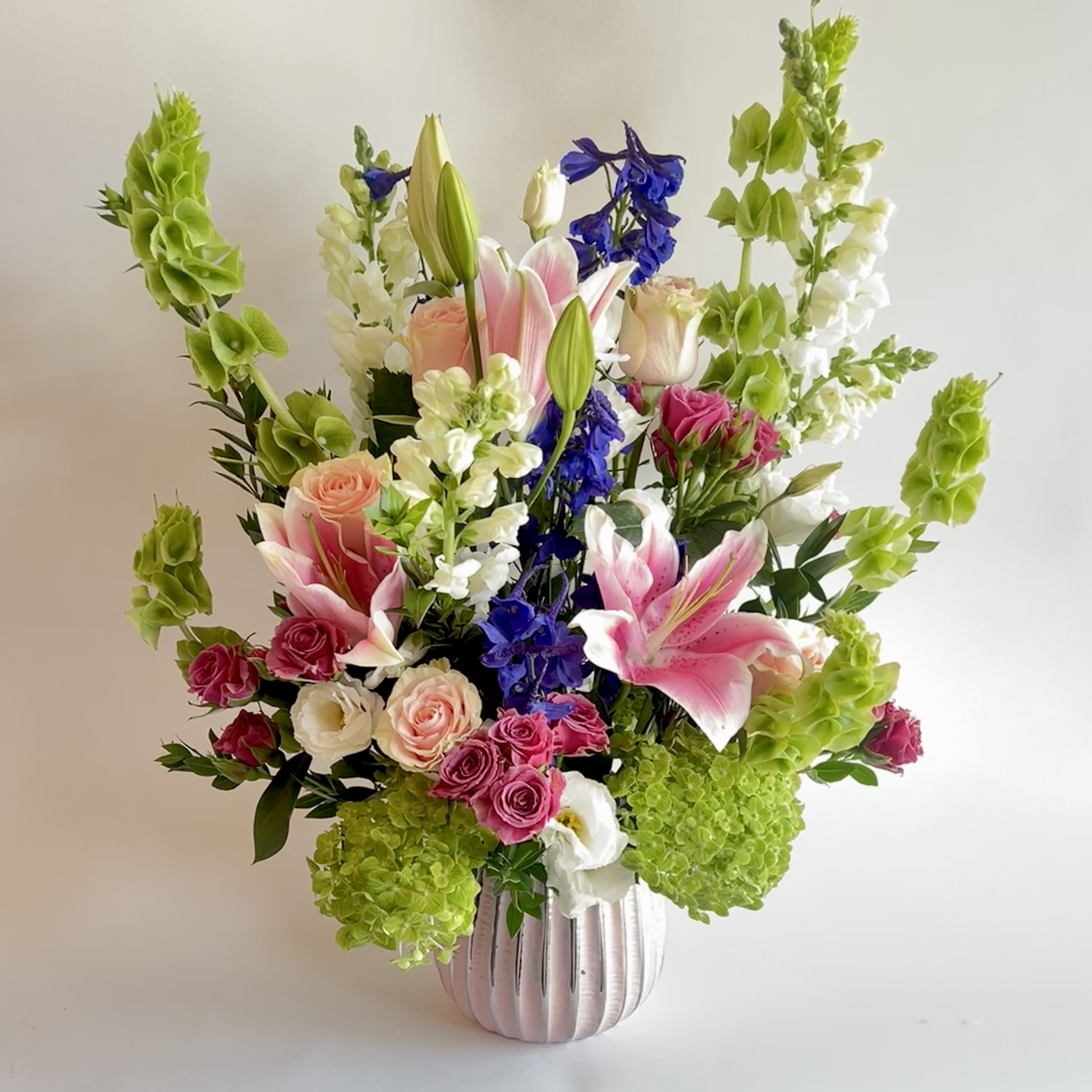 Easy Elegance Easy Elegance - Tall draping arrangement filled with roses, hydrangeas, lilies, and bells of Ireland. In beautiful pastel colors.