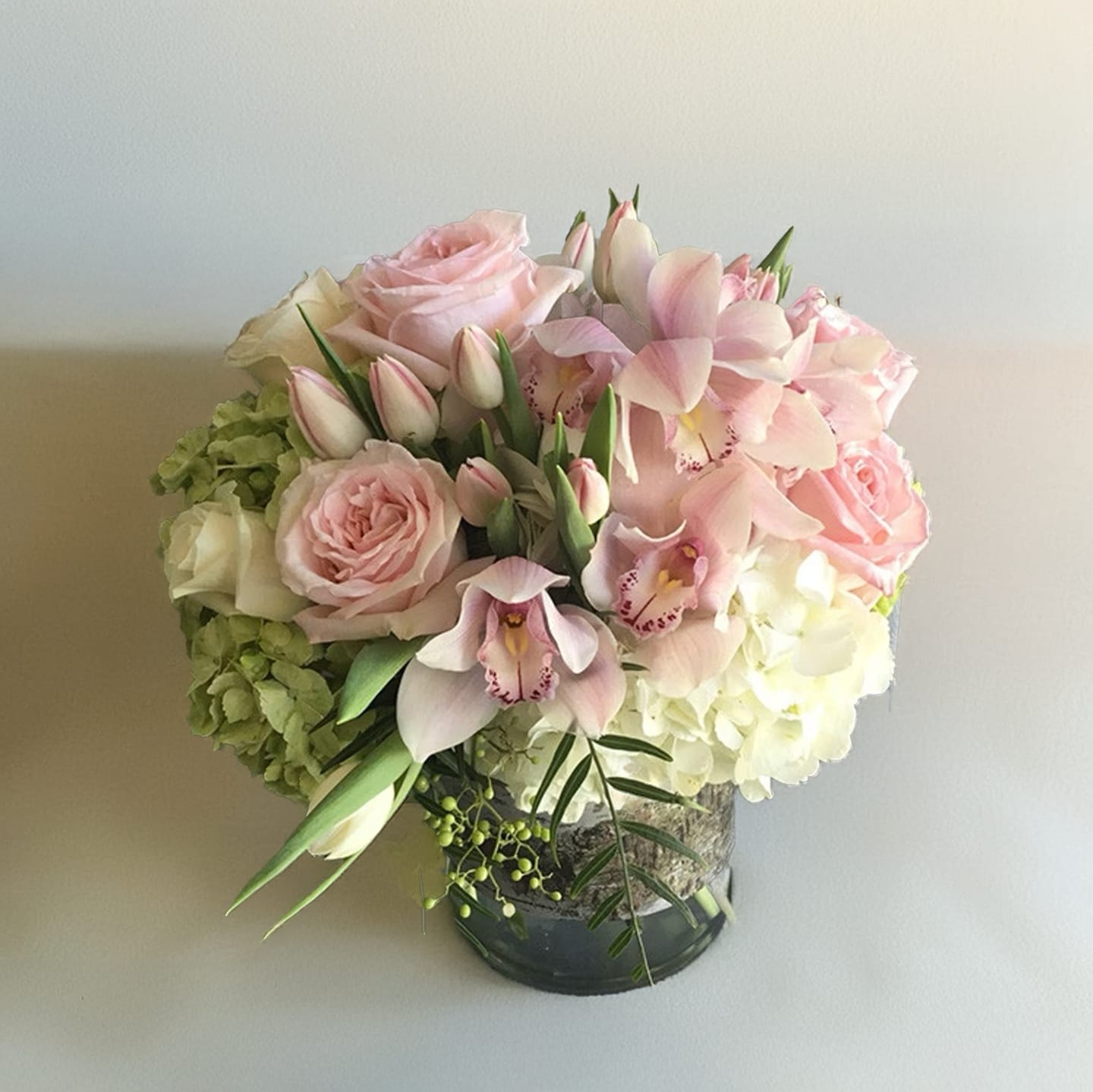 Dainty Delight  - Elevate your space with this stunning, compact floral arrangement. A harmonious blend of delicate white hydrangeas, soft pink roses, and exquisite pink cymbidium orchids and tulips create a picture-perfect bouquet. This arrangement measures approximately 15&quot; wide and 15&quot; tall, making it the ideal centerpiece or gift for any occasion.