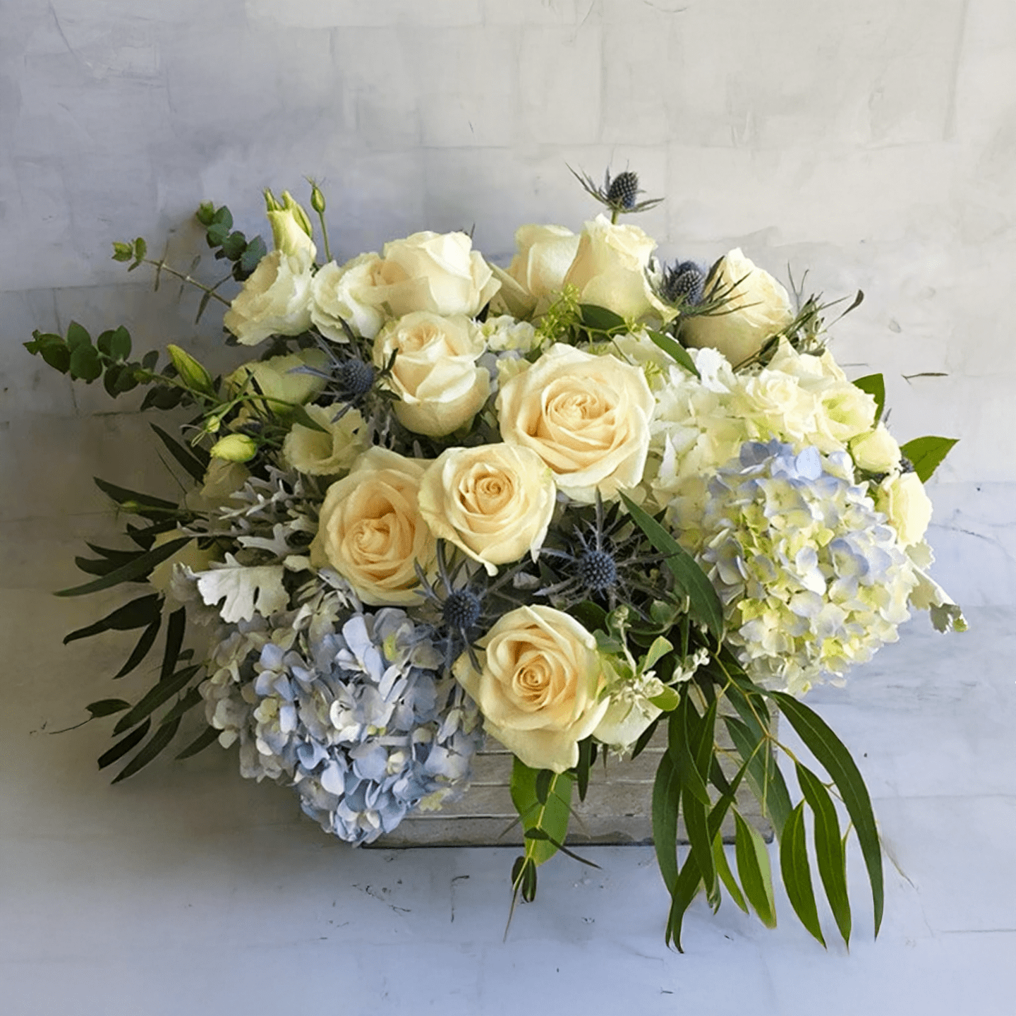 Ocean Eyes Ocean Eyes - Blue hydrangeas and white roses in a wooden box.