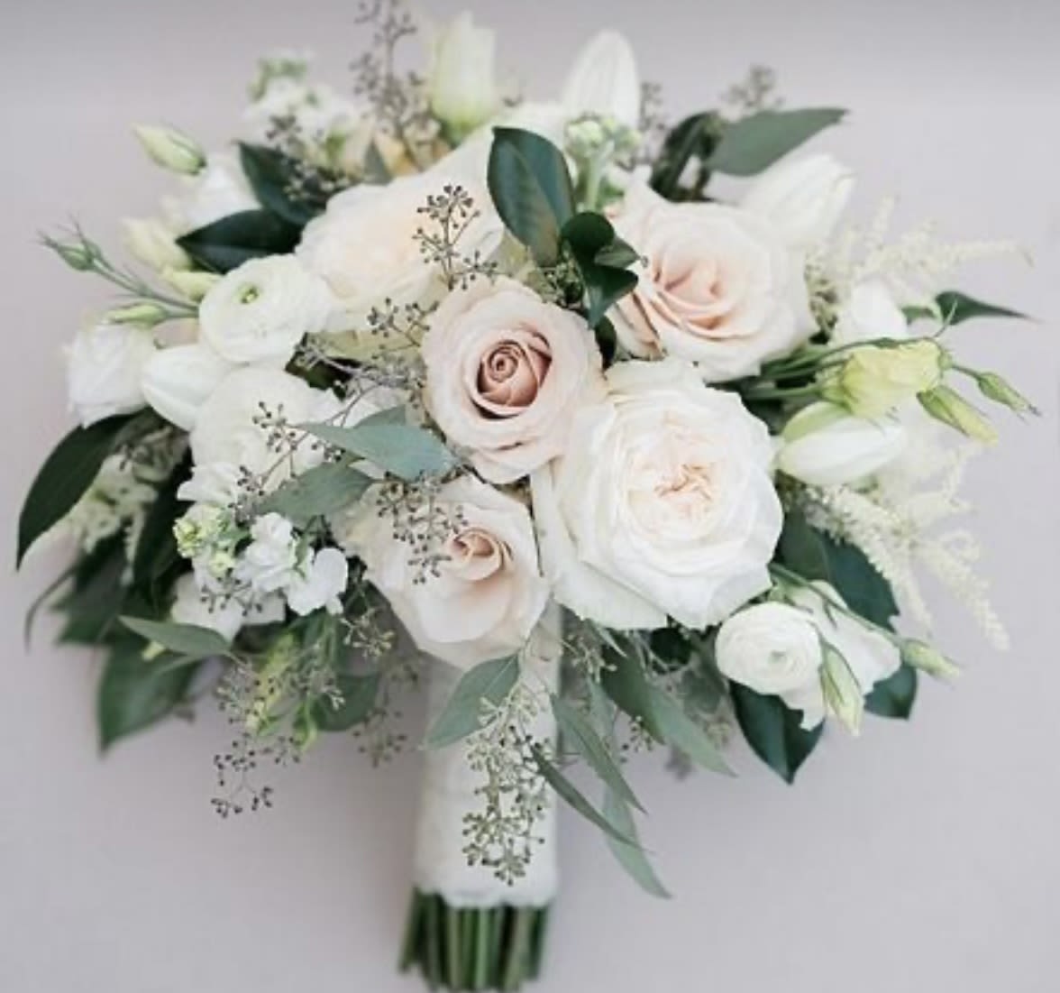 Blush Ivory Elegance Bridal Bouquet Blush Ivory Elegance Bridal Bouquet - Delicate, romantic, and timeless — the Blush Ivory Elegance Bridal Bouquet is a dreamy arrangement of soft blush and creamy ivory roses, crisp white lisianthus, ranunculus, and tulips, nestled among silver-toned eucalyptus and lush seasonal greenery. Hand-tied with a satin ribbon, this bouquet is perfect for the classic or modern bride who desires understated luxury with a soft, ethereal touch. Ideal for weddings with a neutral, blush, or garden-inspired palette. Custom color options available upon request.