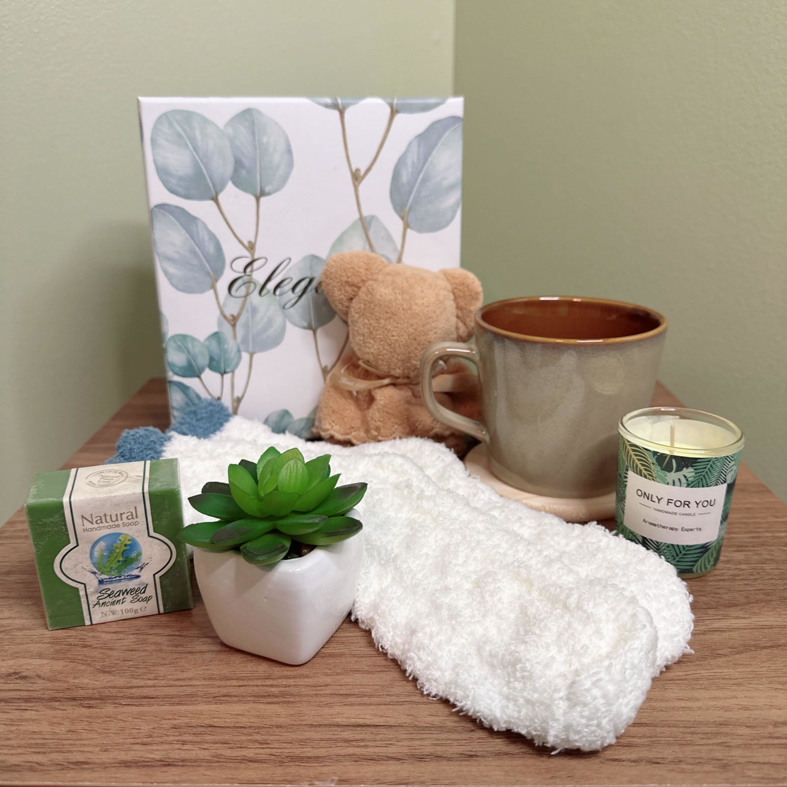 Elegance Gift Set - Indulge in the ultimate relaxation experience with our Elegance Gift Set, carefully curated to provide a serene and rejuvenating escape. This thoughtful collection includes:  - A soothing candle with a calming scent, perfect for unwinding after a long day - A plush white socks, soft against your skin and ideal warming up your feet - A beautiful silk succulent plant, adding a touch of natural elegance to any room - A bar of natural handmade soap, crafted with love and care to nourish and moisturize your skin - A charming folded towel teddy bear, providing comfort and companionship - A stunning mug, perfect for sipping your favorite hot beverage while enjoying some me-time  This gift set is perfect for anyone looking to treat themselves or a loved one to a little luxury and relaxation. Whether it's a birthday, anniversary, or just because, our Elegance Gift Set is sure to delight.