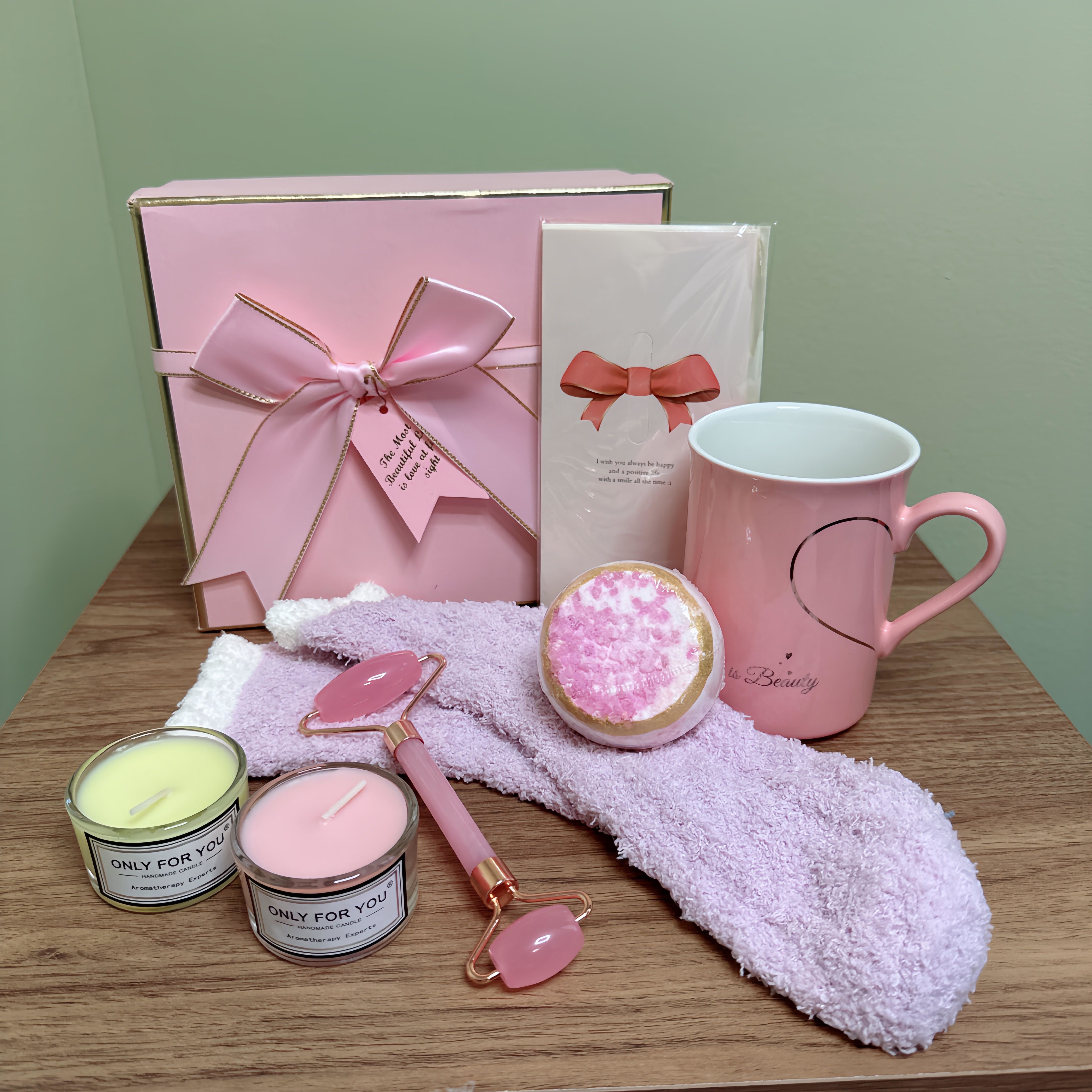  Pamper and Relax Gift Set - Carefully arranged on a wooden table against a light green wall. The items include:  - A pink gift box with gold trim and a large bow - A white card with a pink bow and illegible text - A pink mug with a heart-shaped handle and the word &quot;Beauty&quot; written on it - Two candles in small glass jars with labels that read &quot;Only for You&quot; - A pink rose quartz facial roller - A pink bath bomb - A light purple towel  This gift set is designed for self-care and relaxation, with items that promote pampering and wellness. 