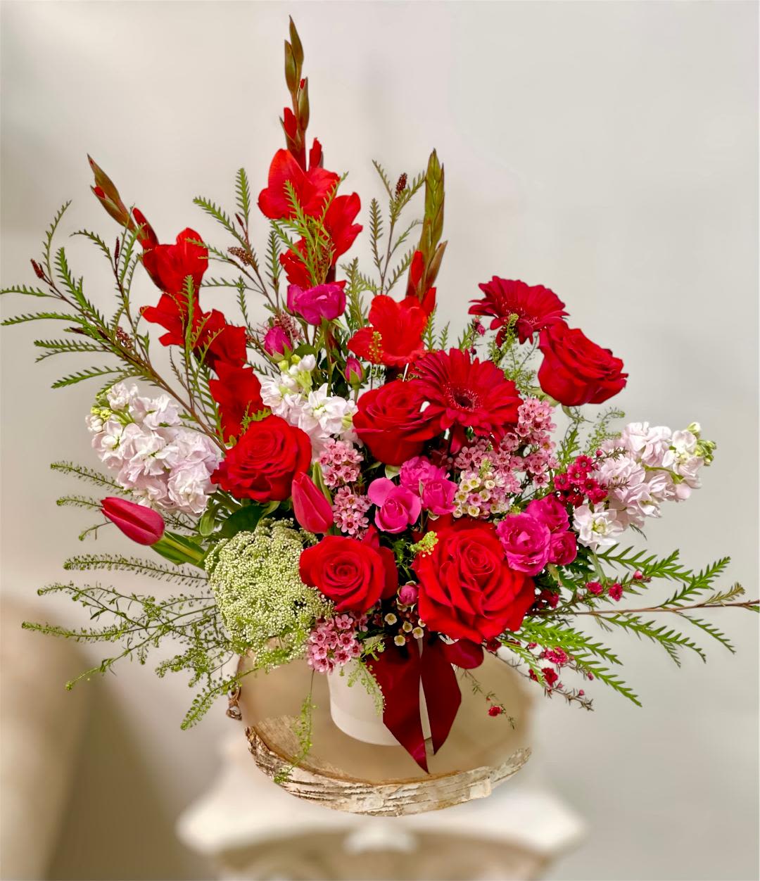 Lovely Wink - Product Information Theme Colors: Shades of Red &amp; pink  Featured Blooms: Roses, Gerbera, Tulips, spray roses, Gladiolus, Stock, Seasonal Blooms  HK Flowers have a uniqueness of florals and seasonal blooms, certain flowers or colors may not be available as each season affects the availability, color, size, and shape of each floral bloom. Some flowers may be substituted accordingly. arrangement design in Round black box . Photos are used as a reference for the color palette and is NOT indicated of the final product. We ask for your trust in us that we will pick out the best seasonal available blooms, while still capturing the arrangements' theme and colors mentioned above.