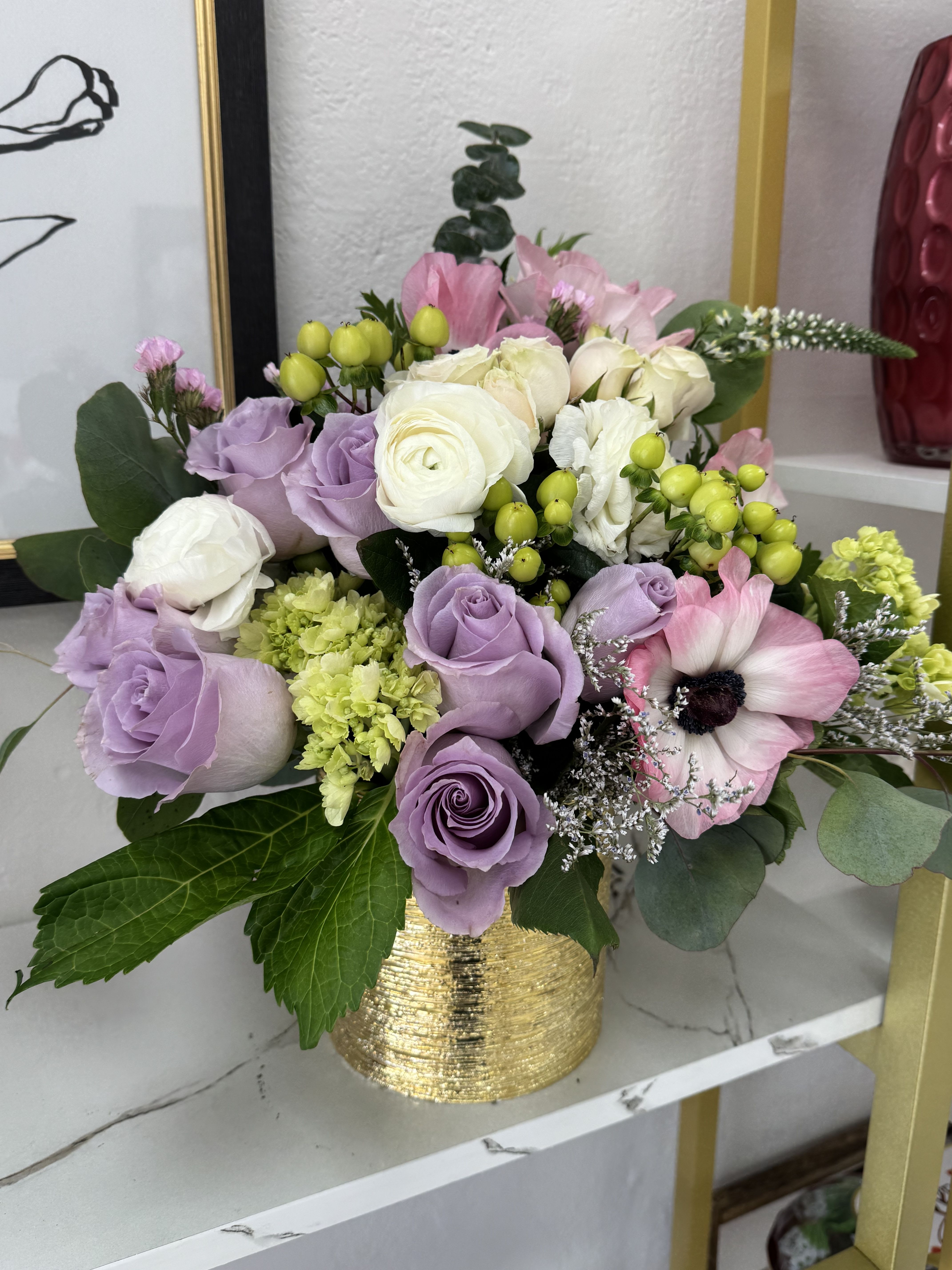 Golden Hours - Este arreglo tiene un aire romántico, delicado y sofisticado, con tonos suaves como lavanda, blanco, verde lima y rosado pastel, todo coronado por esa base dorada elegante.