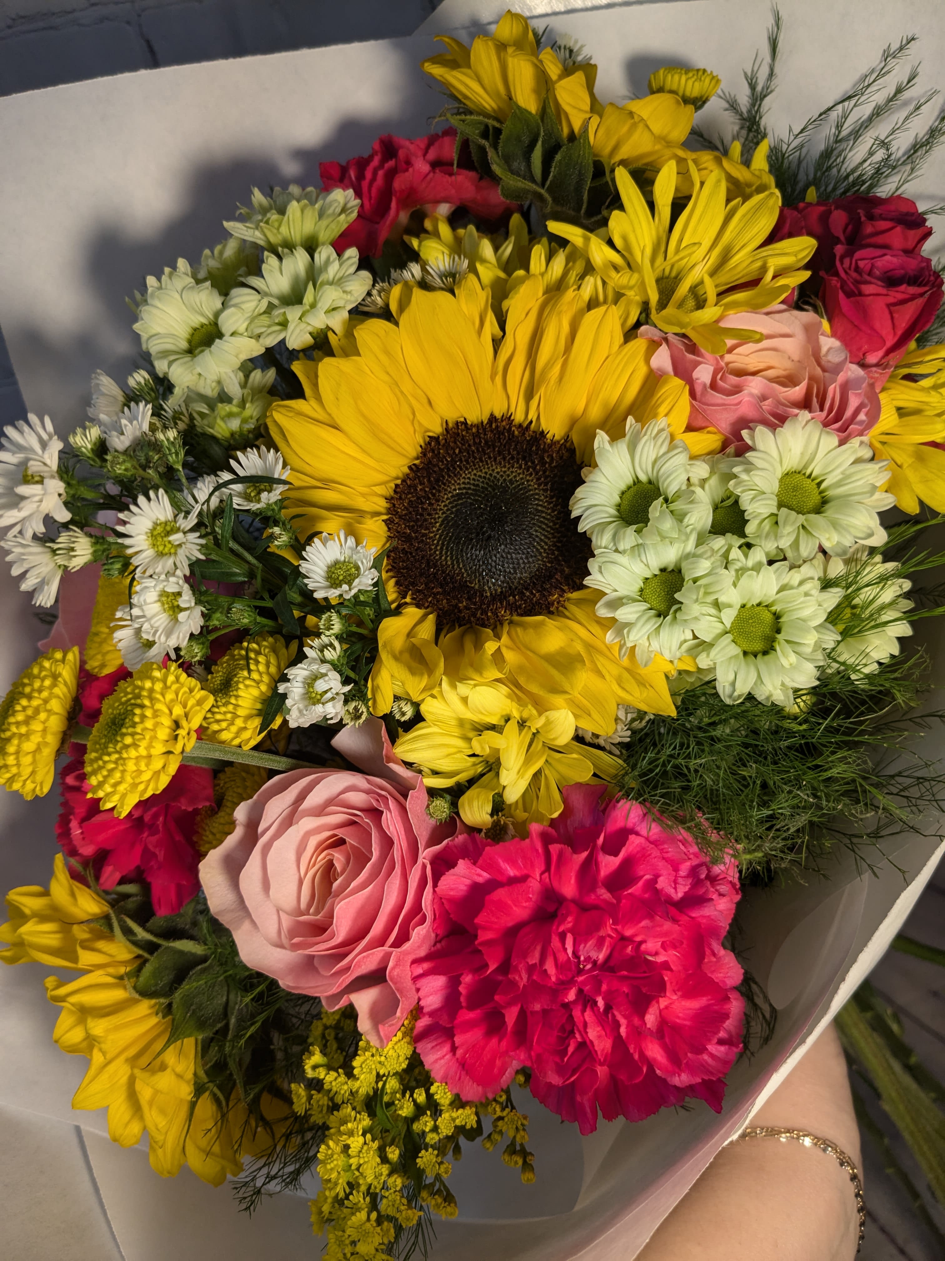 It's Poppin Hand-tied Bouquet - This bright and cheerful hand-tied bouquet features sunny sunflowers, pink roses, hot pink spray roses, adorable daisies, micro daisies, monte, chrysanthemum buttons, and long lasting carnations.  *This is a hand-tied and wrapped bouquet - not a vased arrangement