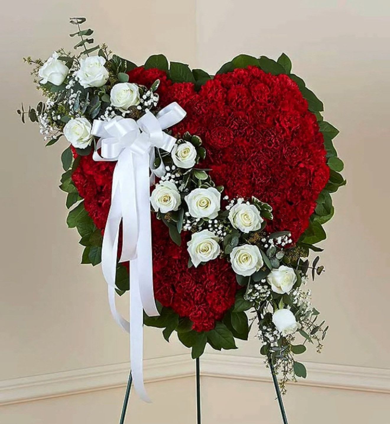 Tribute Heart  - Honor a loved one with a special tribute. Our heart-shaped standing arrangement of fresh red carnations, accented by a cascading sash of white roses adorned with a white satin ribbon, will help you elegantly express your sincere devotion and sympathy.