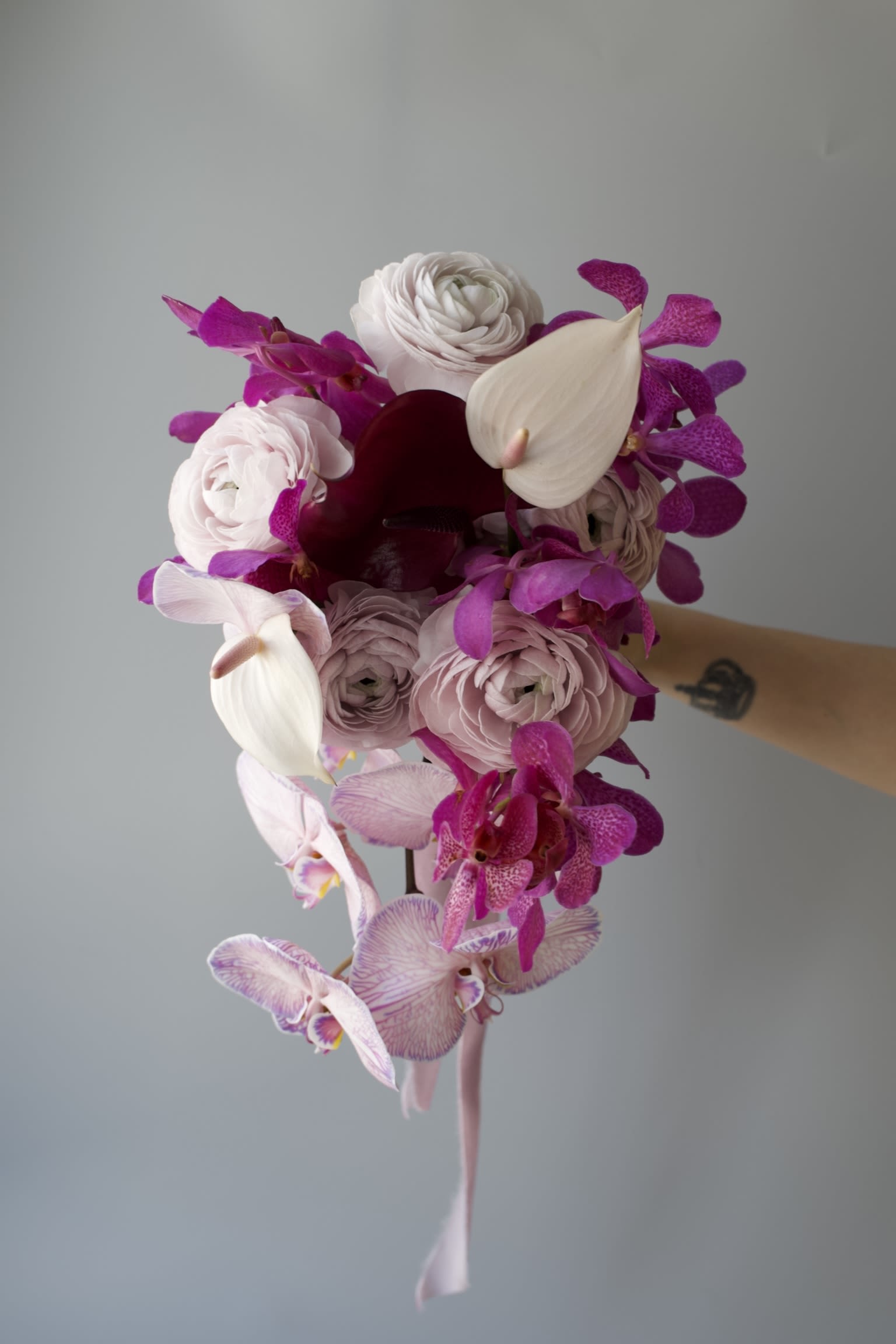 Velvet Bloom - Modern Cascading Bridal Bouquet  A sculptural cascade of refined blooms — designed for the modern bride. Shown in bold tones of blush, fuchsia, and plum, this bouquet features orchids, ranunculus, calla lilies, and anthuriums in a flowing, asymmetrical form.  Available in custom color palettes and flower combinations to match your wedding vision. A true statement piece for brides who want unforgettable florals       