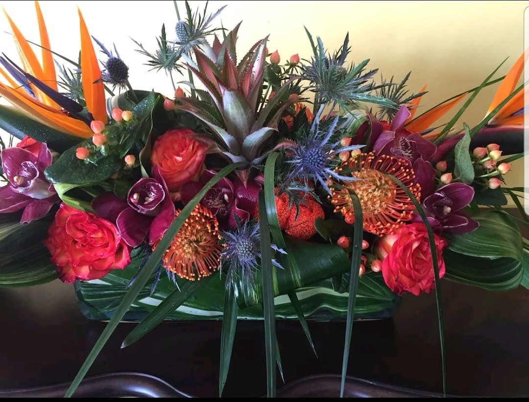 Jungle Fever  - Rectangular glass container covered with tropical leaves filled with seasons best tropical flowers such as miniature pineapples, cymbidium orchids, birds of paradise, blue thistle, pretia, and tropical foliage to complete the look. 