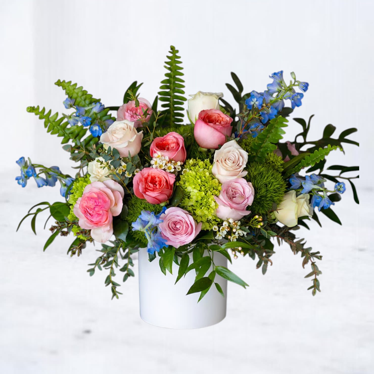 Botanical Daydream - Botanical Daydream is a lush, garden-inspired flower arrangement bursting with color and texture. Designed in a modern white vase, this vibrant bouquet features premium roses in blush, peach, and pink tones, vivid green hydrangea, playful blue delphinium, waxflower, and a mix of tropical greenery and ferns. It's an ideal pick-me-up for birthdays, celebrations, or “just because” moments. Available for same-day flower delivery in Houston, Magnolia, The Woodlands, Tomball, and surrounding areas.