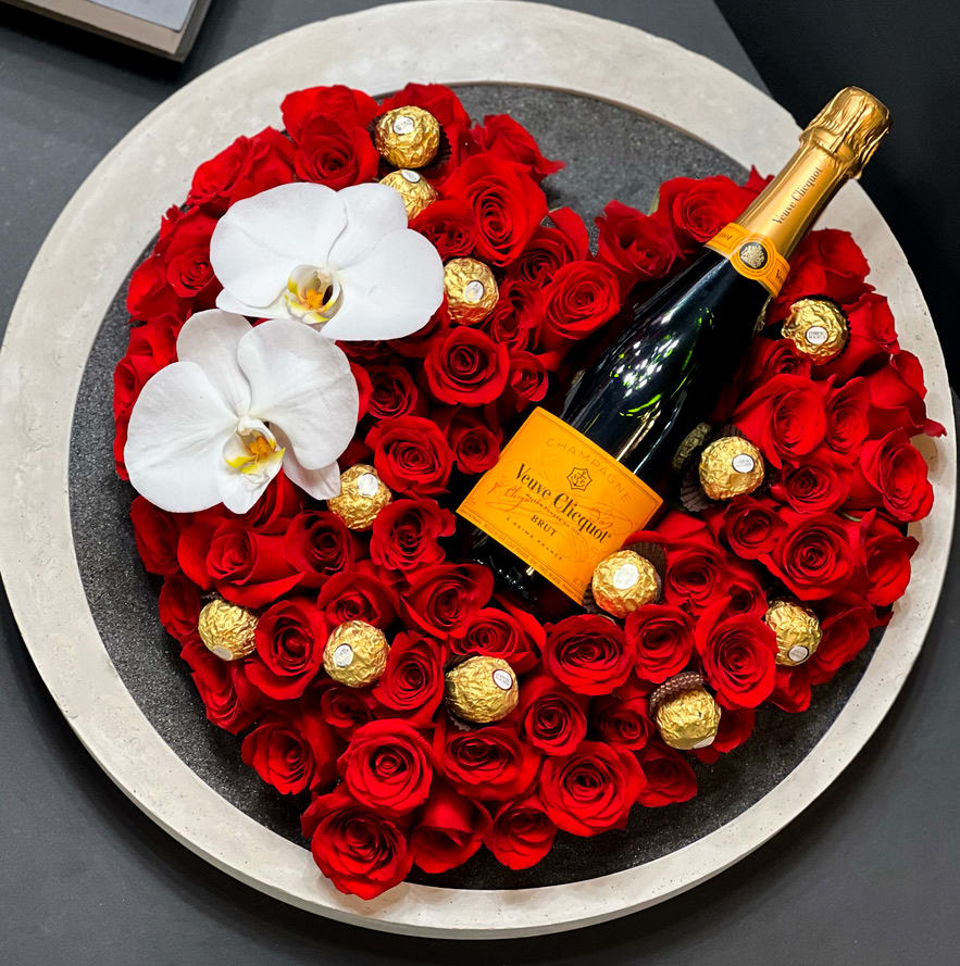 HEARTS AND KISS | RED ROSES ARRANGEMENT IN CUSTOM ROUND TRAY - Product Details: EXTRA LARGE Unique modern arrangement with 100 and above red roses and phalaenopsis orchids in a concrete round hand-made tray. Includes: 100 and above red roses, phalaenopsis orchids, custom-made concrete tray, black sand, Veuve Clicquot Brut Champagne, and Ferrero rocher chocolate Overall size: 20&quot;dia x 5&quot; high. 