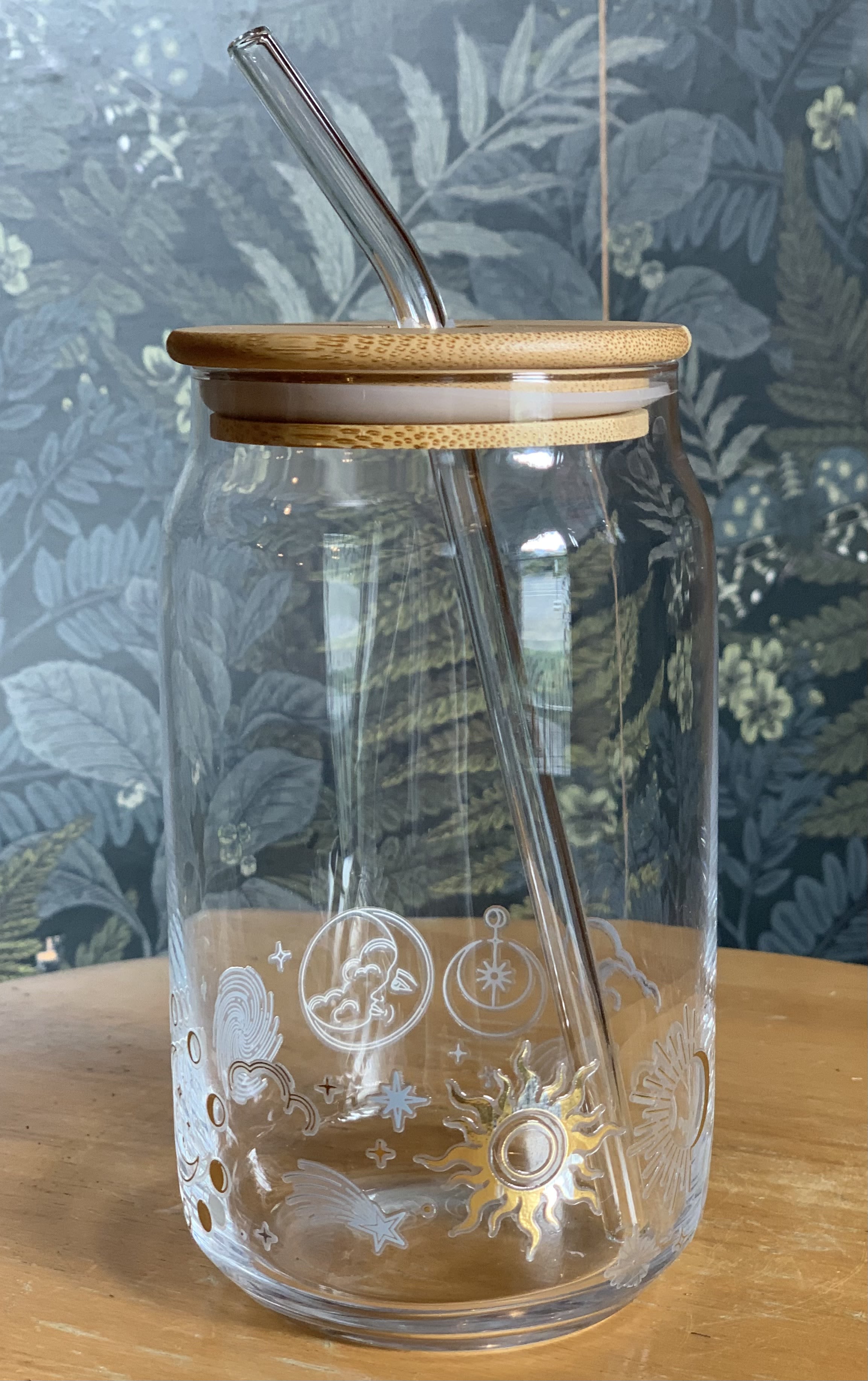 Glass Cup with Lid and Straw - One glass cup with glass straw and bamboo lid. Perfect for those looking for a sustainable alternative. Decorated with a celestial inspired design, with the colors gold and silver. Hand wash only. Limit 4. Designs may vary; subject to current availability. 