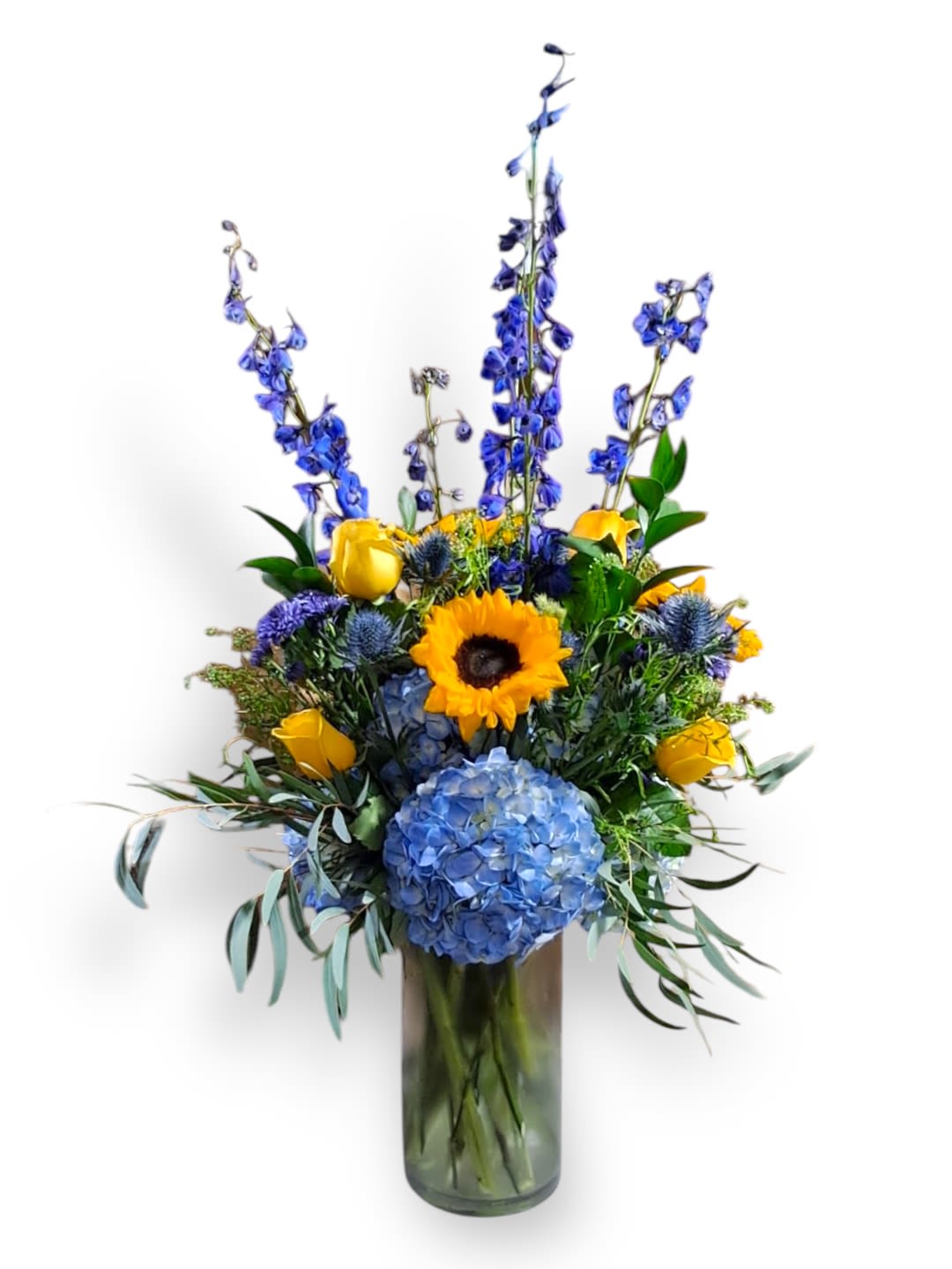 Summer Breeze Summer Breeze - This gorgeous arrangement has delphiniums, sunflowers, roses, hydrangeas, thistle, cushions, and greens in a tall 12 “ glass vase that has a 6 “ opening.